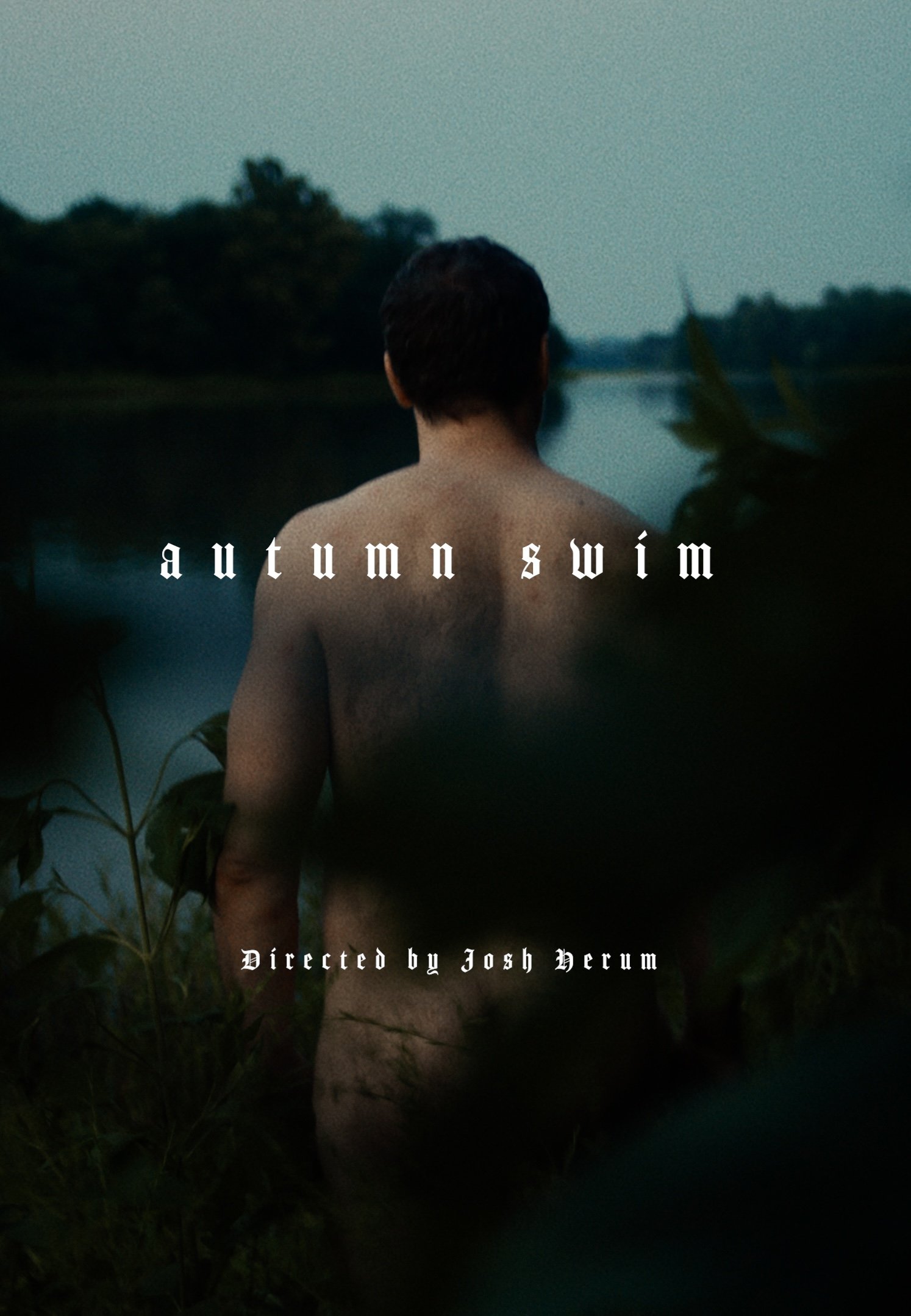 A person with short dark hair is standing outdoors near a lake during dusk, facing away from the camera. The scene is surrounded by greenery with a calm water body in the background. Overlaid text reads 'autumn swim' and 'Directed by Josh Herum'.