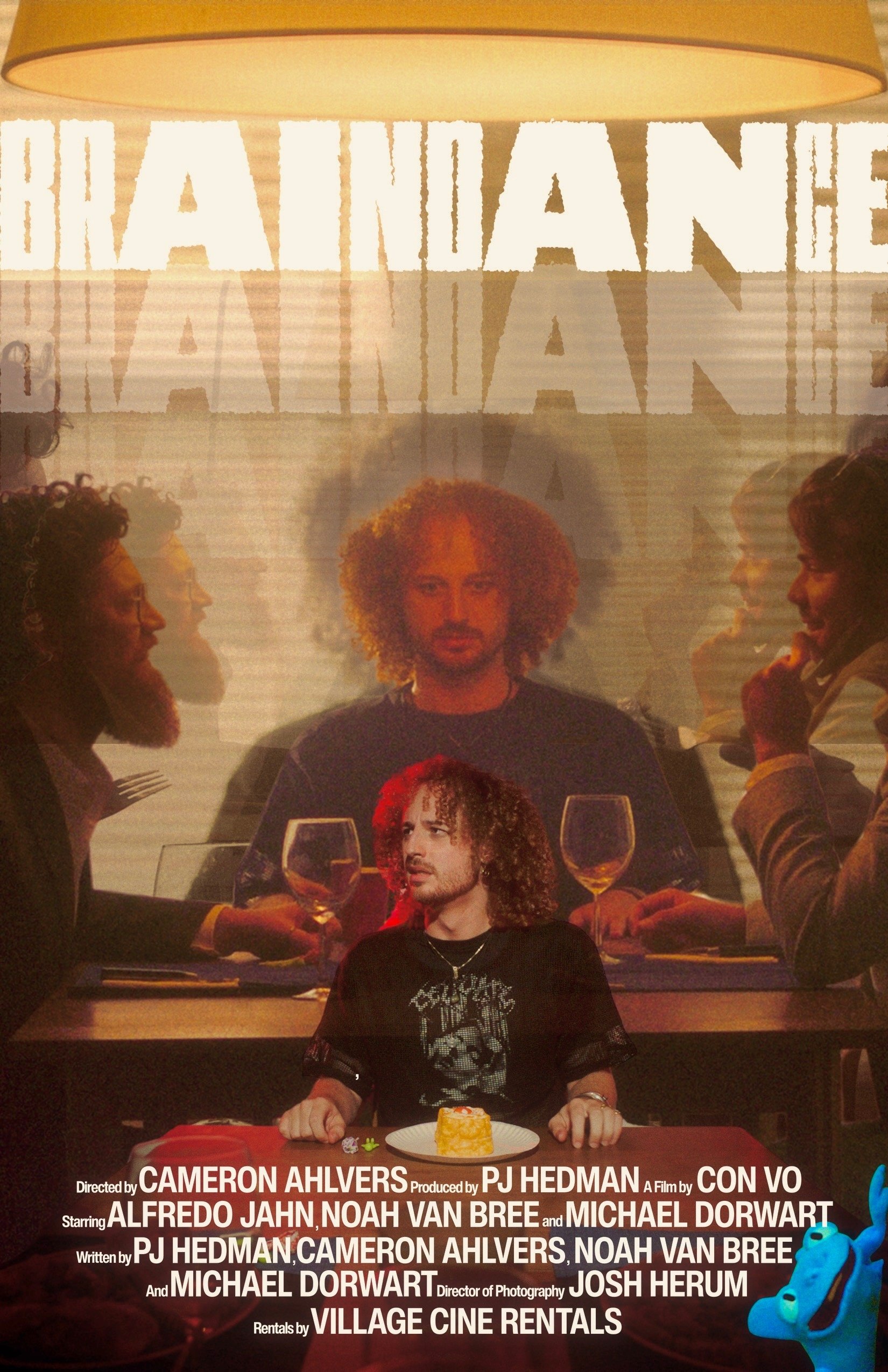 A person with curly hair sitting at a table with a small cake, with a large movie poster or screen behind them showing multiple people at a dining table
