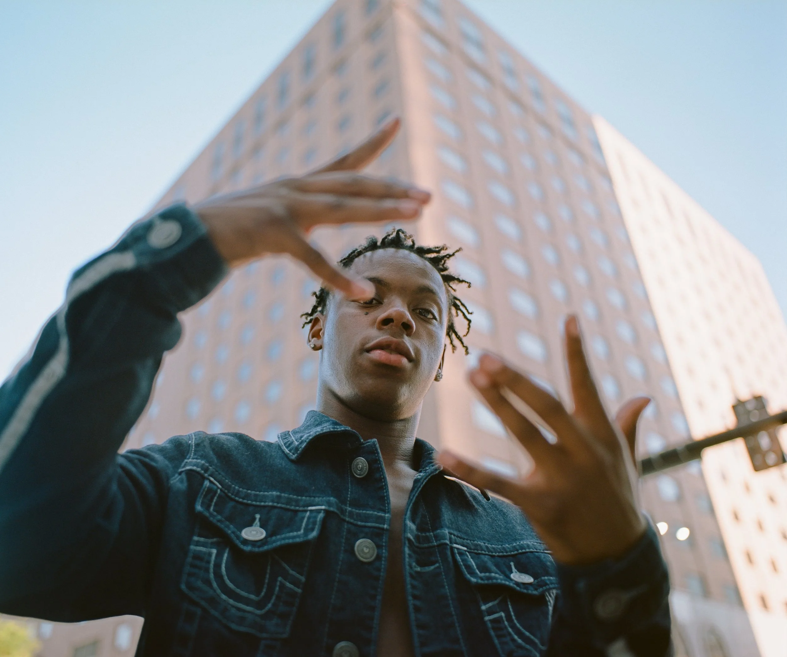 Young man with dreadlocks posing in front of a tall building in an urban environment.
