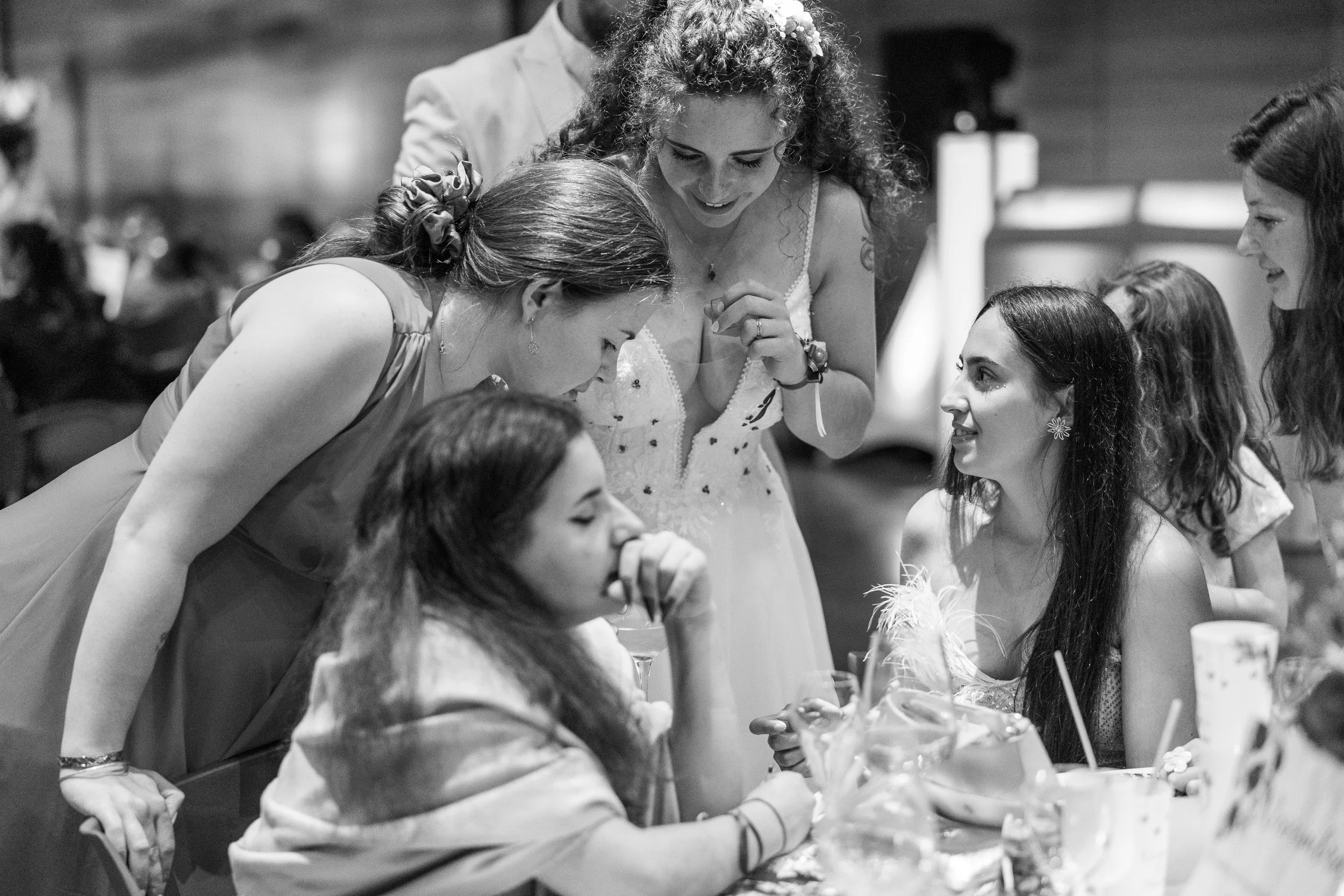 Une groupe de jeunes filles et de femmes sont en train de discuter et de rire lors d'un événement social, probablement un mariage ou une fête, dans un décor intérieur.