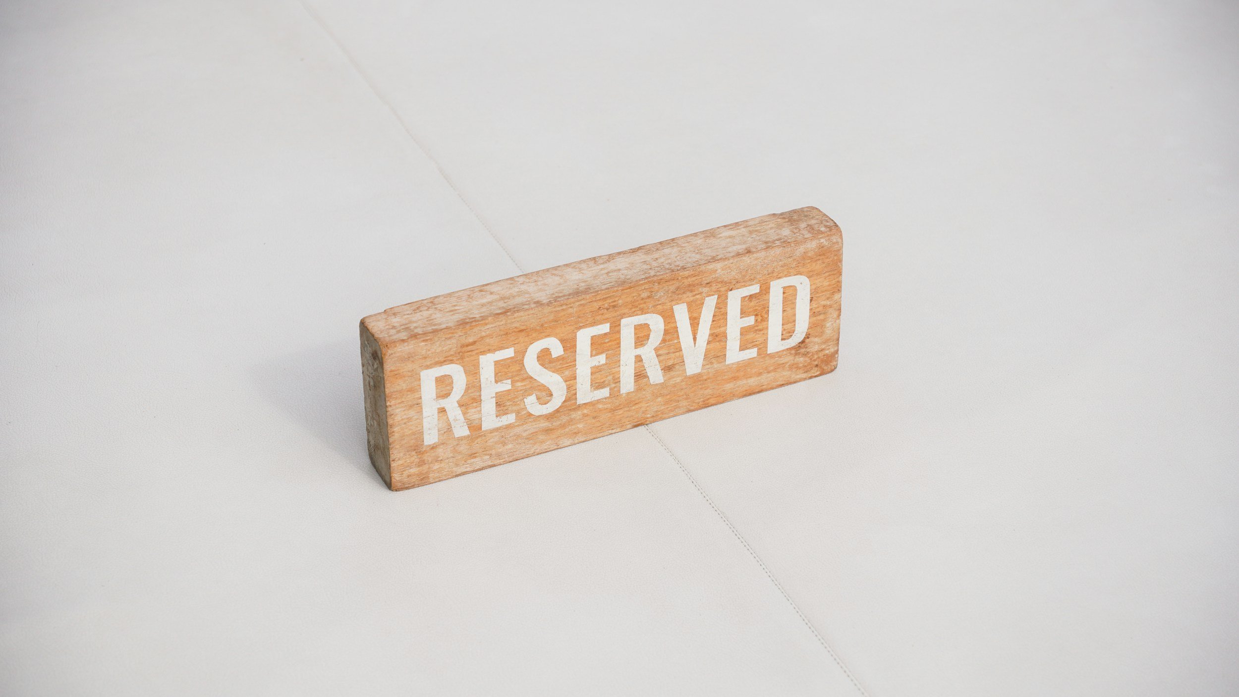 A wooden sign with the word 'RESERVED' on a table in a dimly lit setting, with blurred colorful lights in the background.