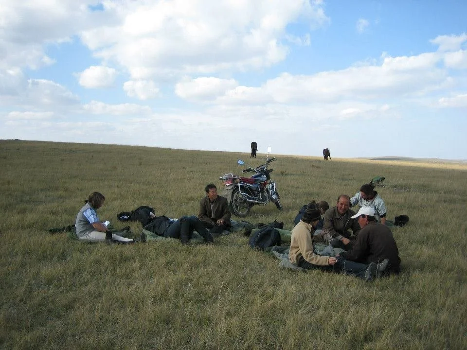 Group of people sitting on grassy field with motorcycles, under cloudy sky