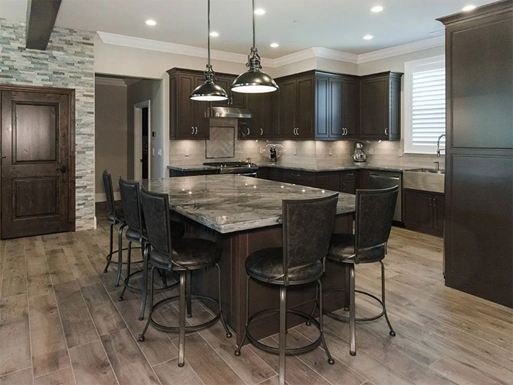 Modern kitchen with dark wood cabinets, marble island with barstools, and wood flooring.