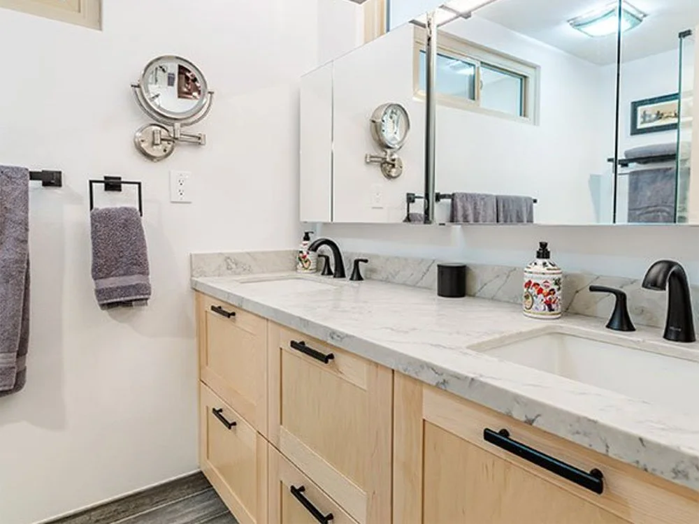 Modern bathroom vanity with marble countertop, black fixtures, and light wood cabinets, with a mirror and purple towels.