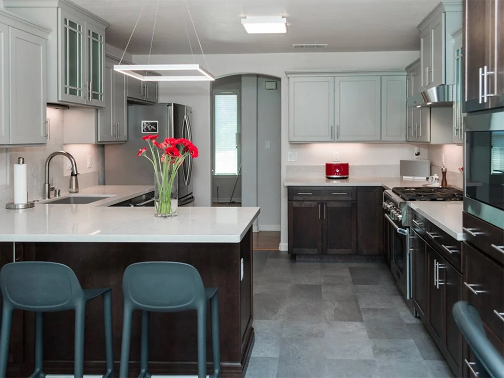 Modern kitchen with gray and dark wood cabinets, a kitchen island with red flowers, stainless steel appliances, and a small red appliance on the counter.