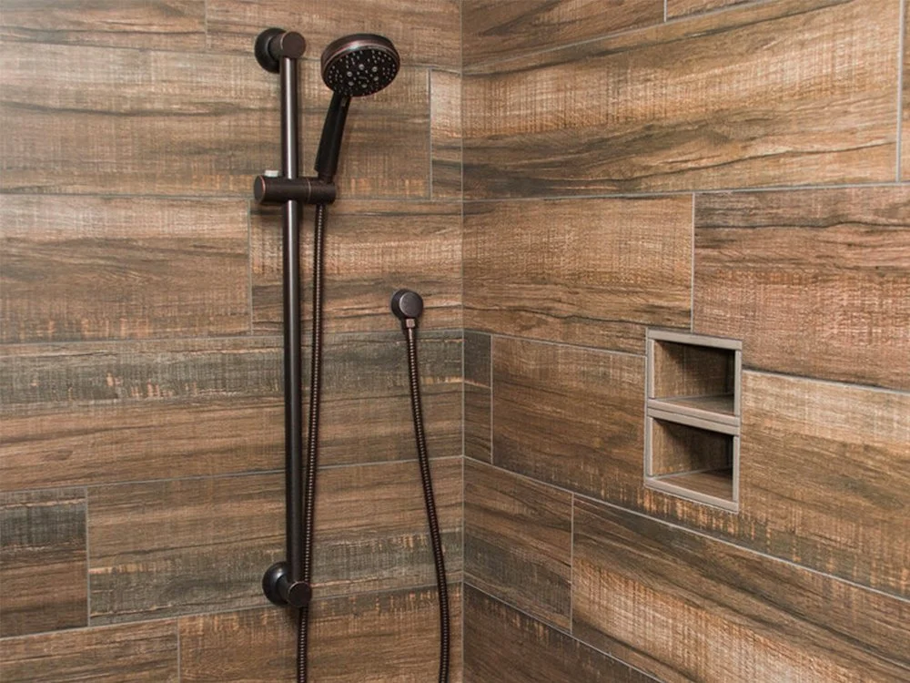 Shower area with wood-look tile walls, a black handheld showerhead, and a built-in wall niche for toiletries.