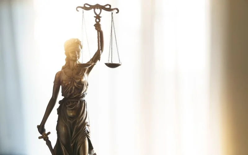 A bronze statue of a woman holding scales in her left hand and a sword in her right. The background is bright and warm.