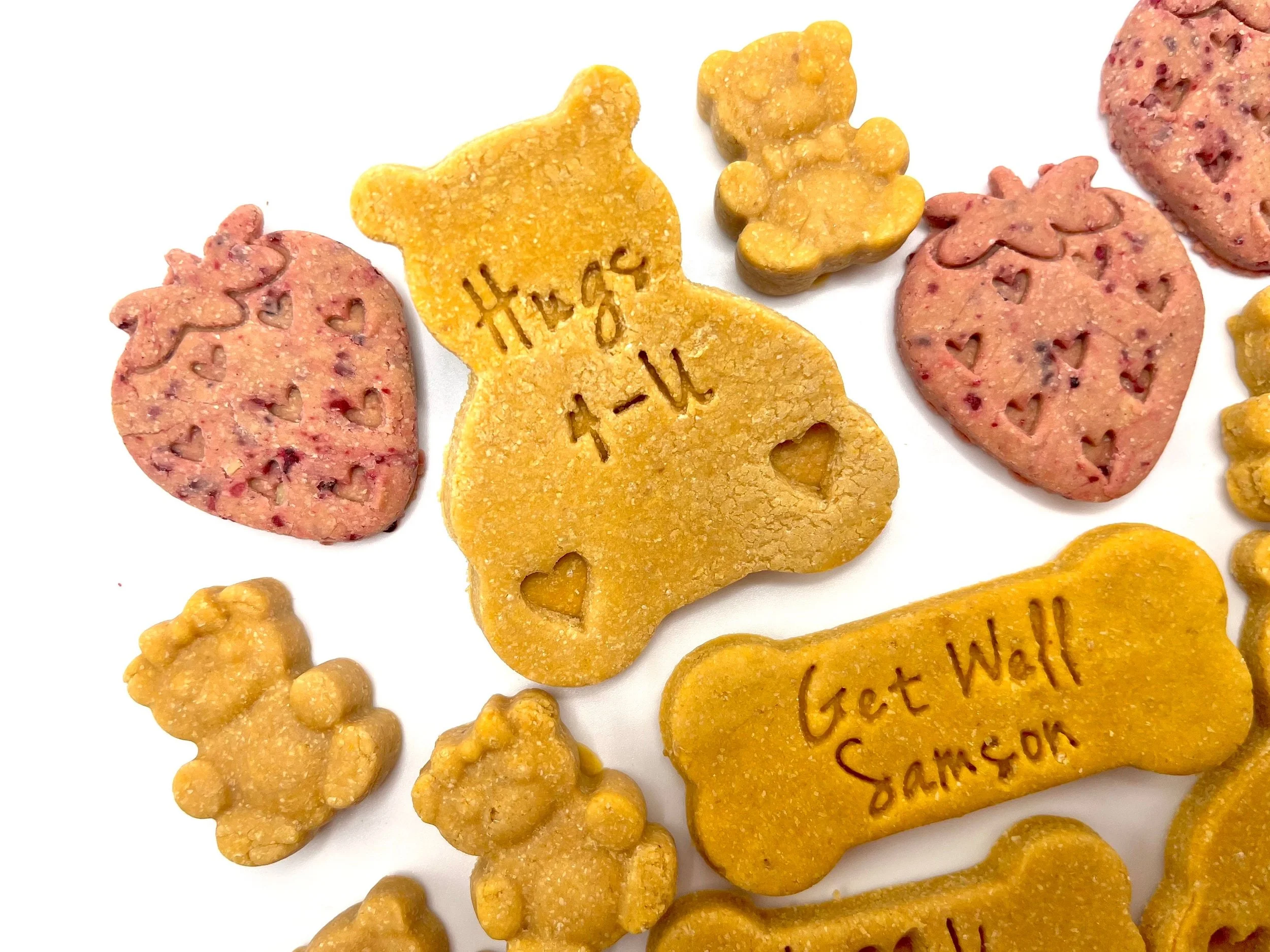 Assorted dog cookies, including a bone-shaped one with "Get Well Sampson" written on it, teddy bear-shaped, and heart-shaped with heart cutouts.
