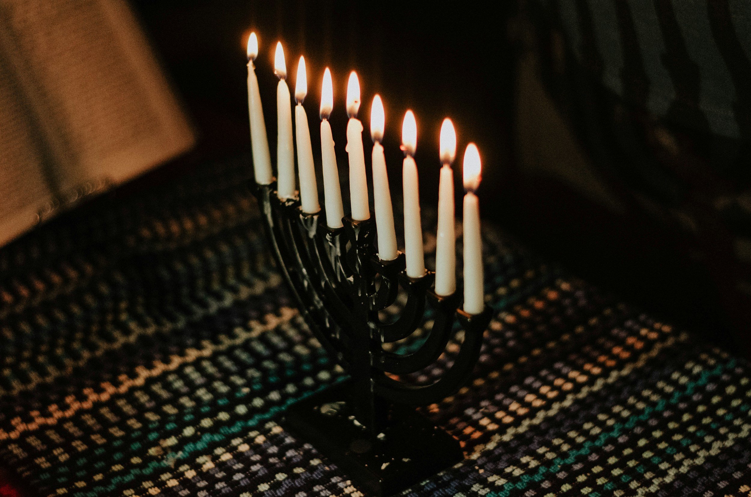 Menorah with nine lit candles on a colorful woven tablecloth.