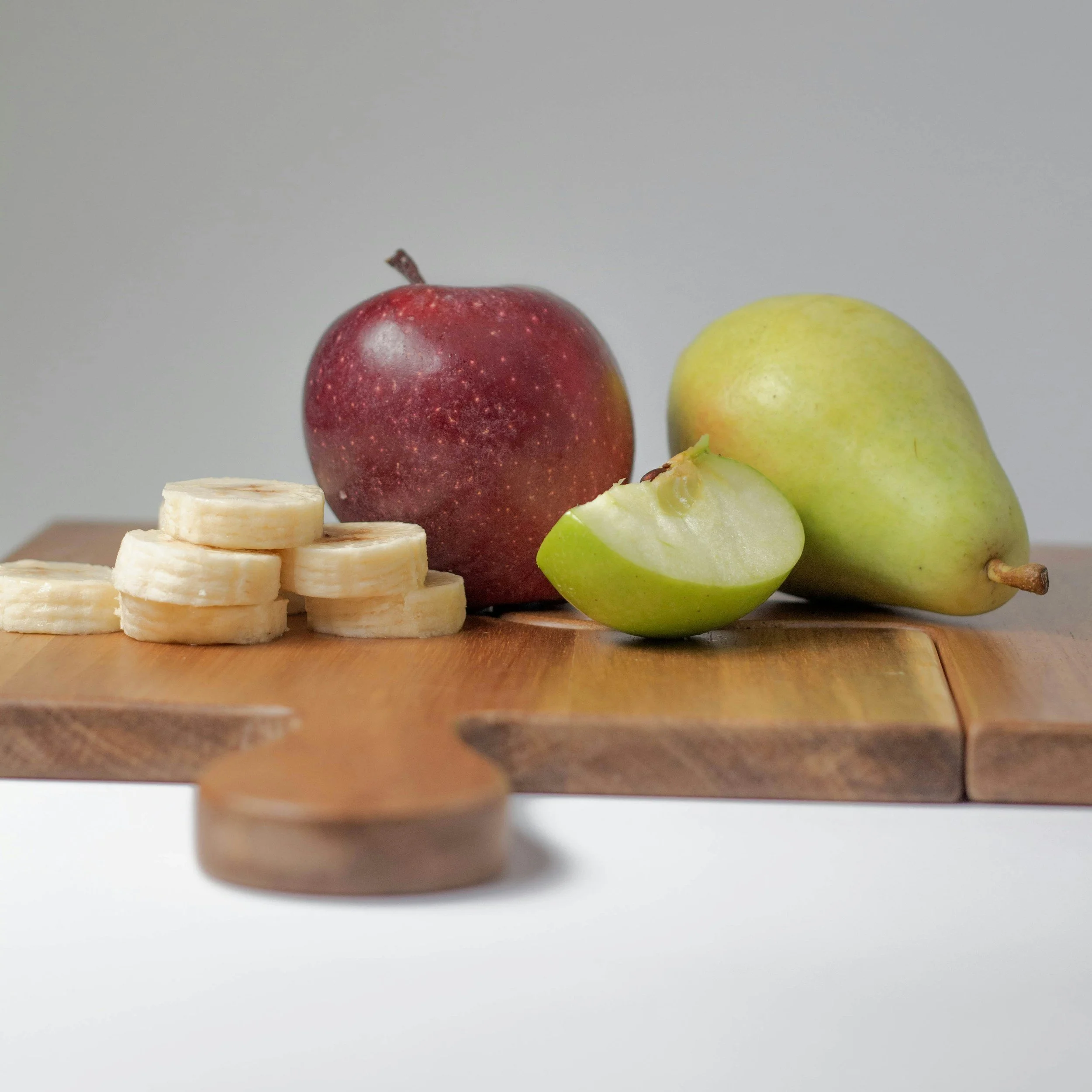 Sliced banana, apple, and pear on a wooden cutting board.
