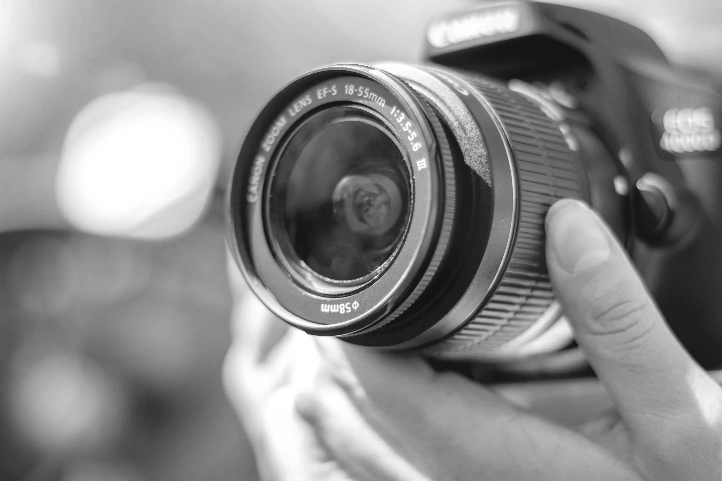 Black and white photo of a person's hand holding a Canon camera with a zoom lens.