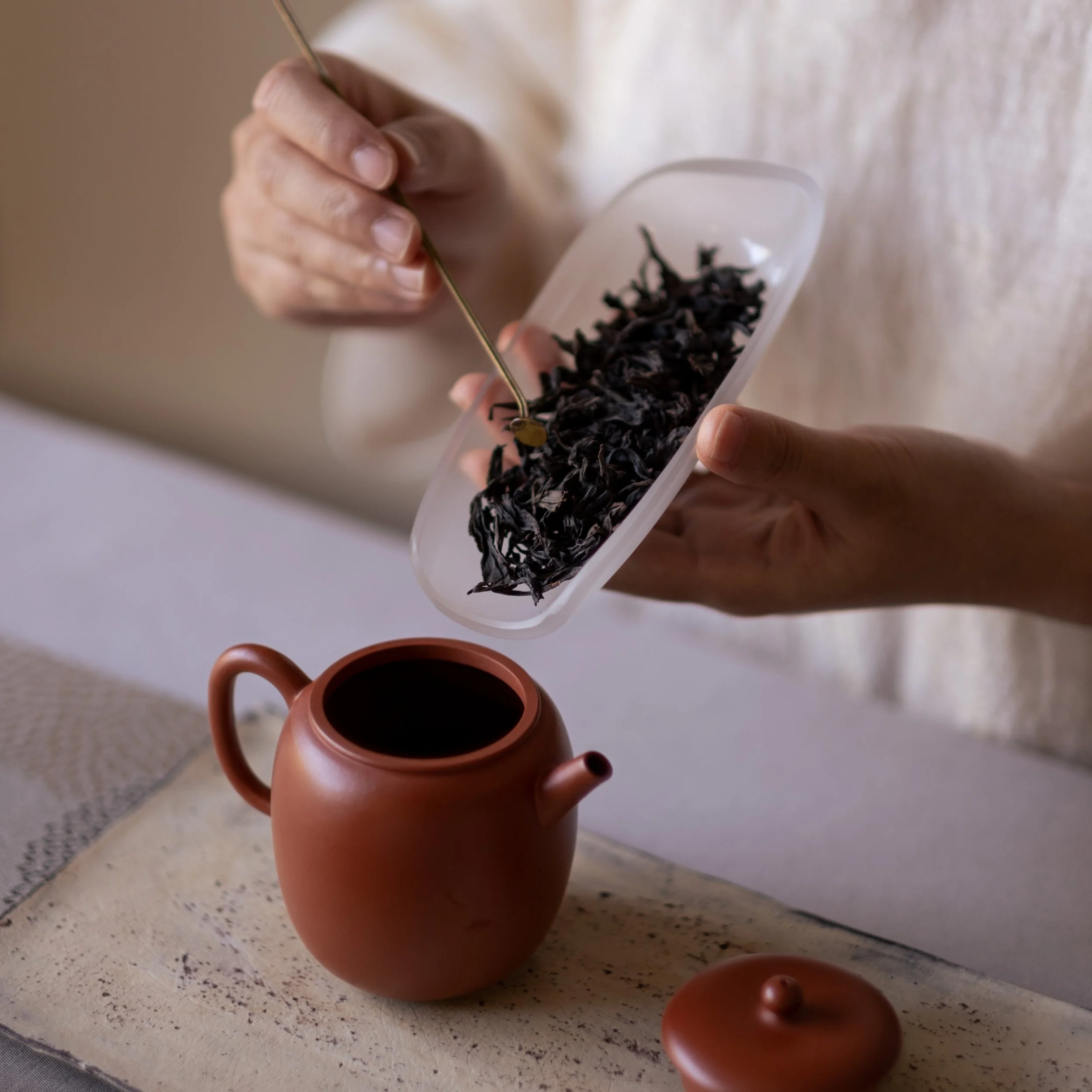 Dry Chinese tea leaves being guided from a tea leaf holder into a clay teapot for Gongfu brewing.