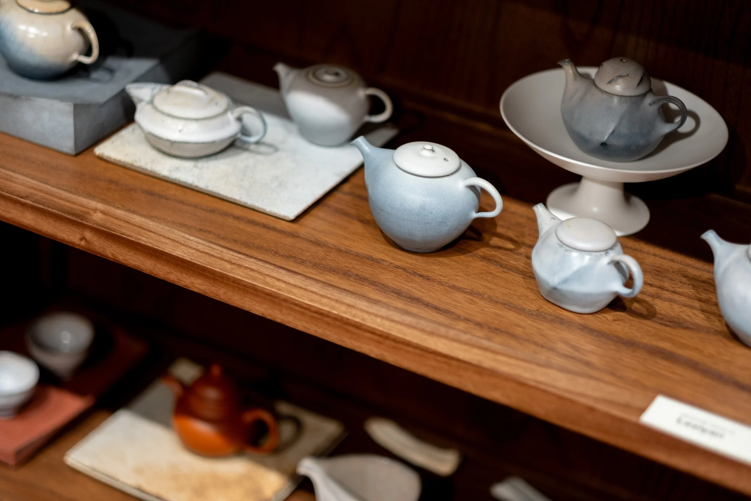 Handcrafted teapots and other teaware displayed on wooden shelves at Teasthetic's NYC Tea Studio.