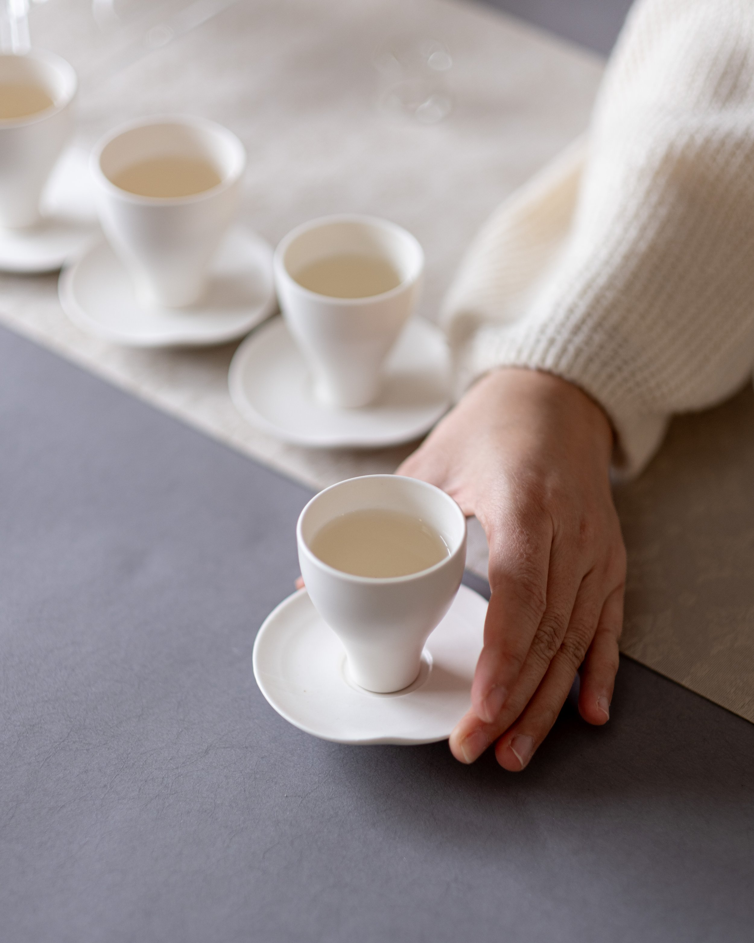 A hand places a white teacup on a saucer during a Chinese tea ceremony.