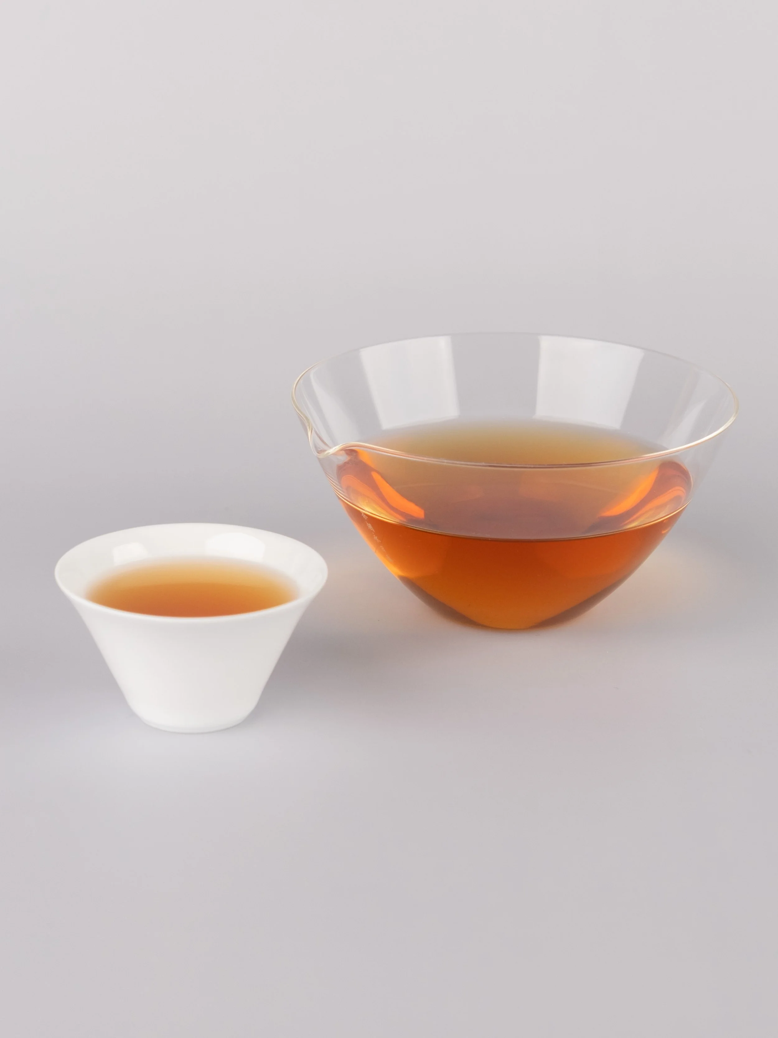 Amber tea liquor in a glass faircup and white porcelain teacup.