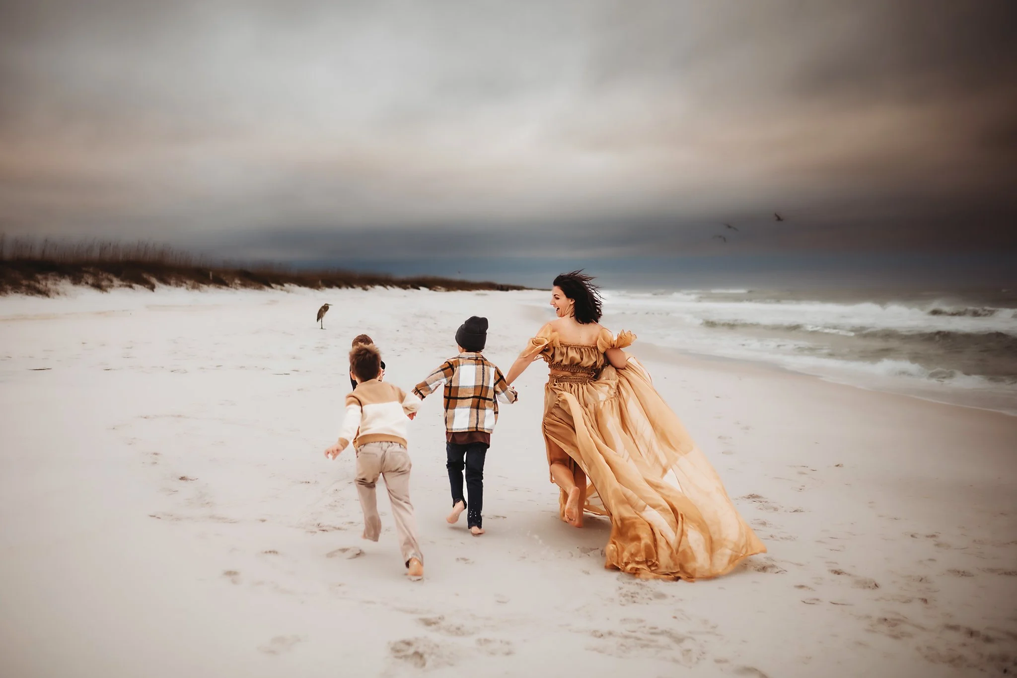 A mother runs on the beach with her three sons as her dress flows in the wind. Taken by Destin Photographer June Sunrise Photography.