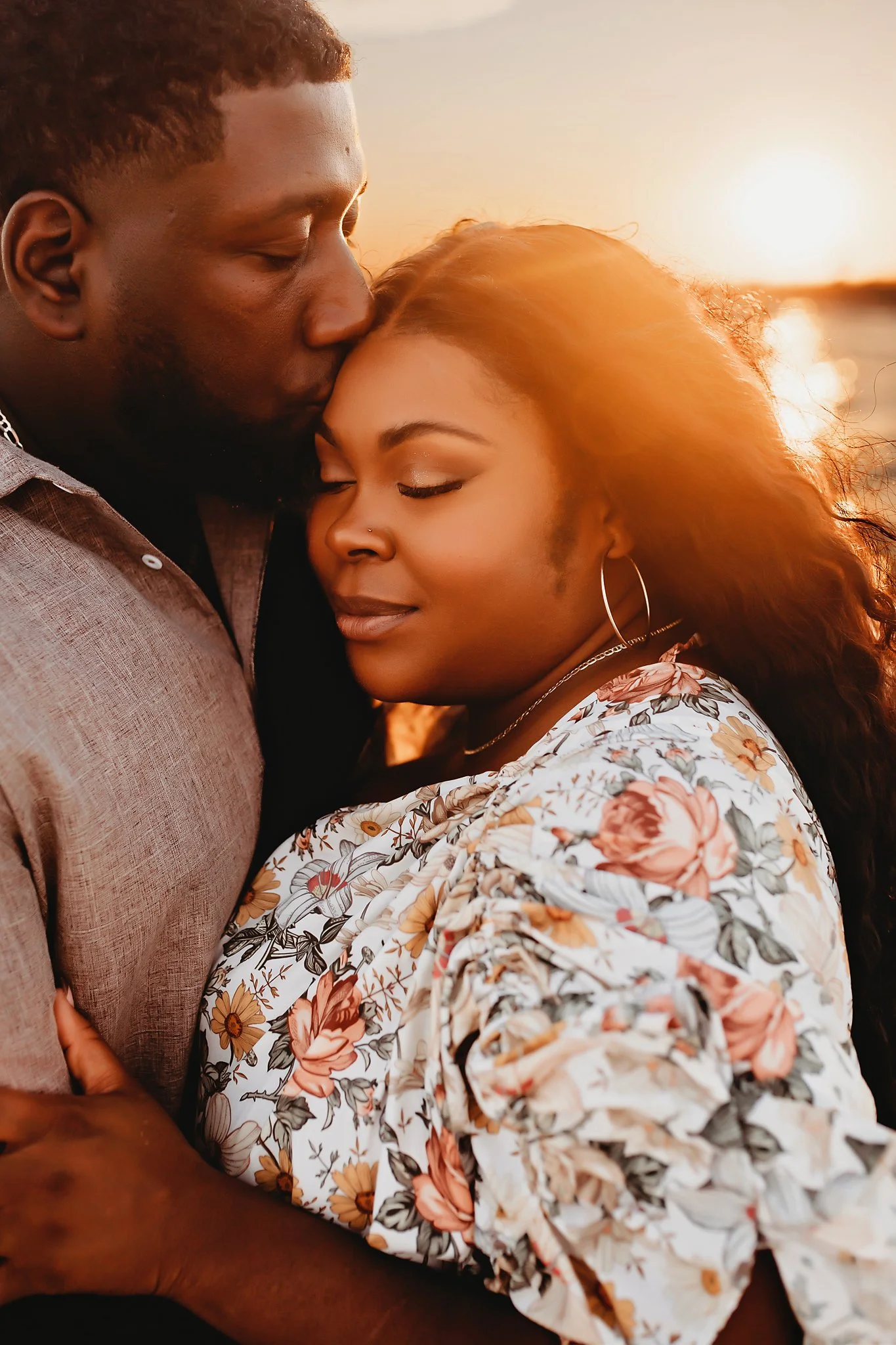 A mother and father pose for couples portraits in front of a golden sunset on Pensacola Beach, Florida. Taken by Pensacola Photographer June Sunrise Photography.