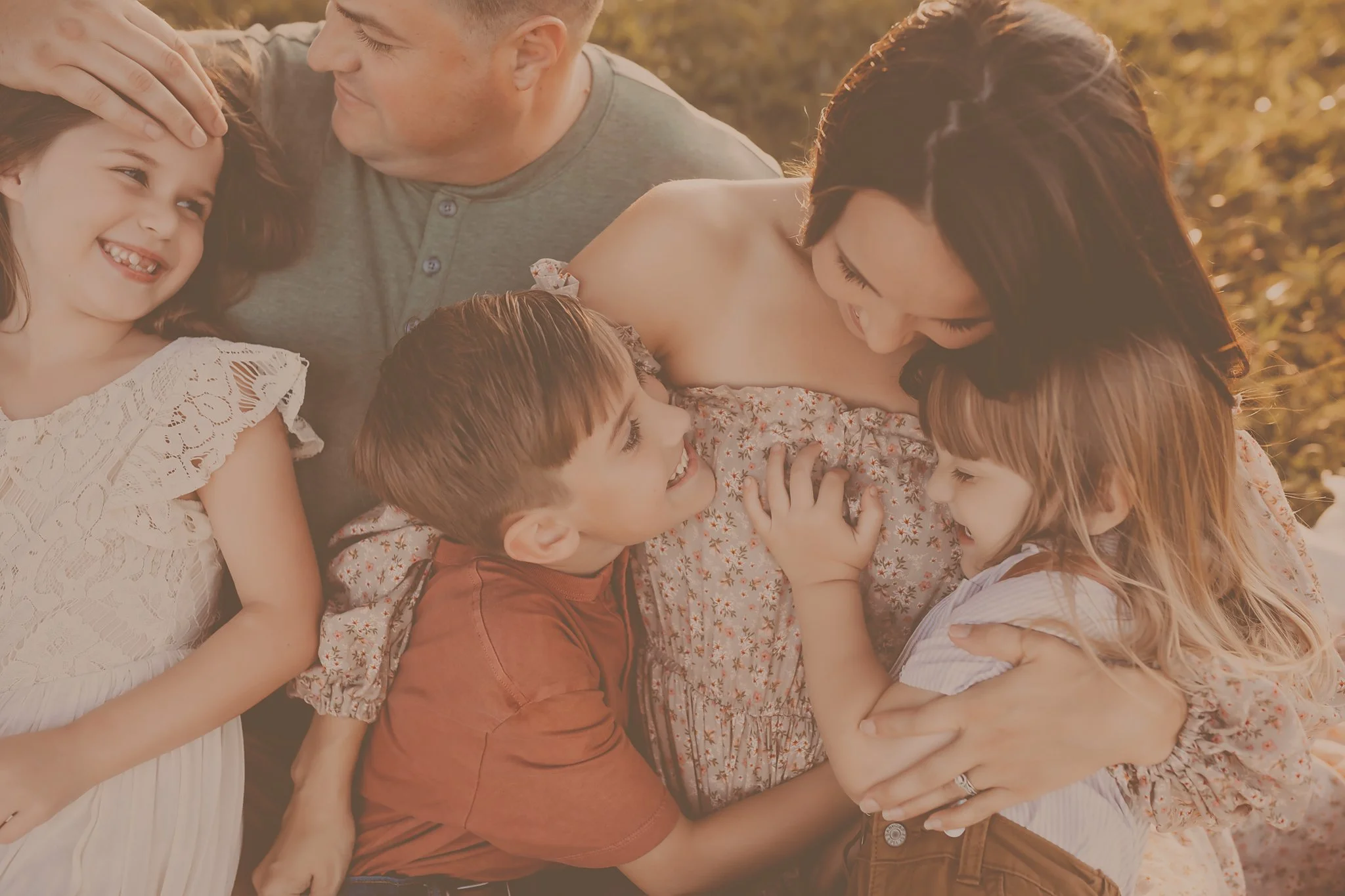 A family snuggles up on the ground together while hugging tightly and smiling at each other. Taken by Pensacola Photographer June Sunrise Photography.