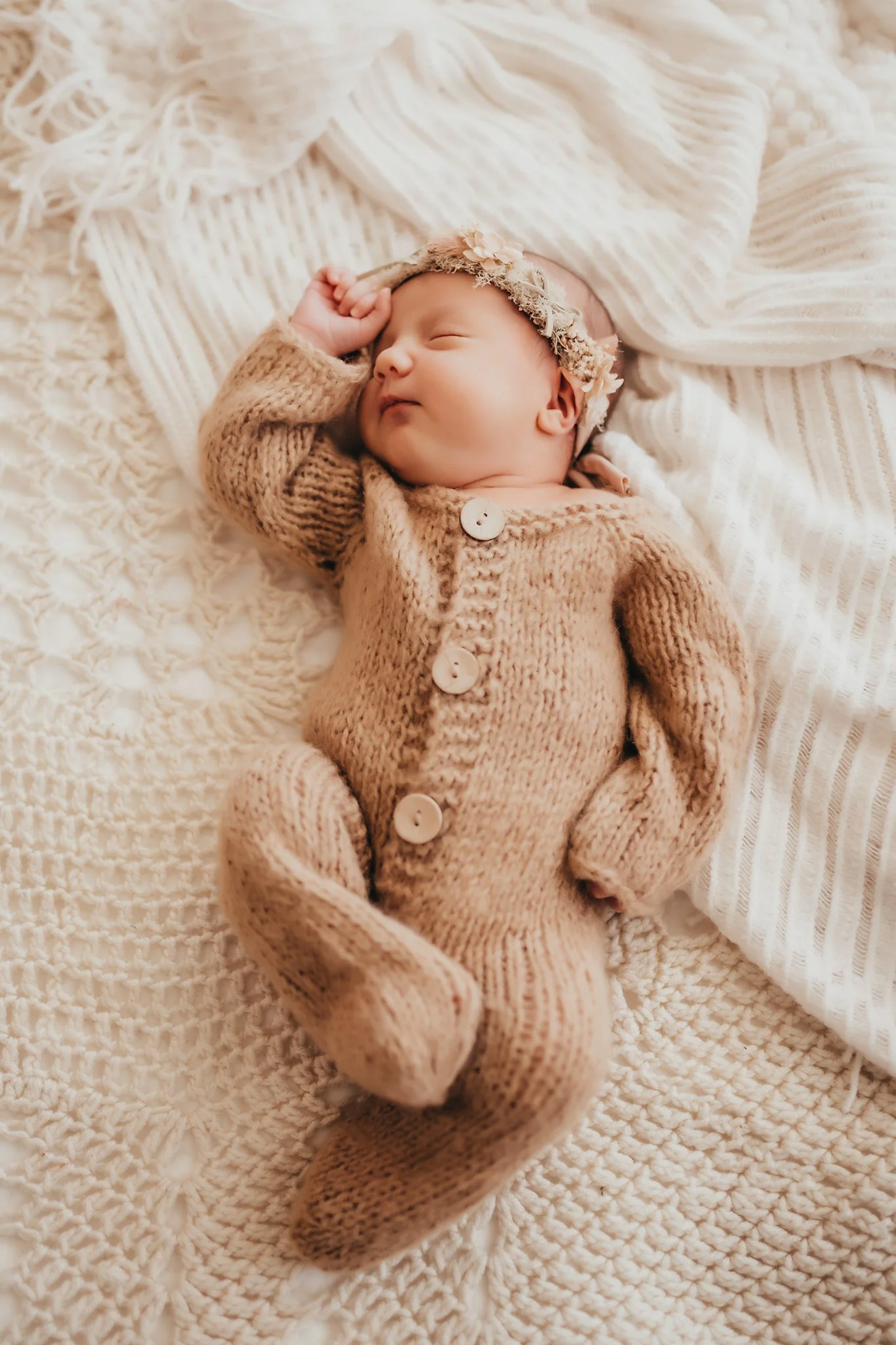 A newborn baby girl sleeps in a knitted onesie with a floral headband. Taken by Pace Florida Newborn Photographer June Sunrise Photography.