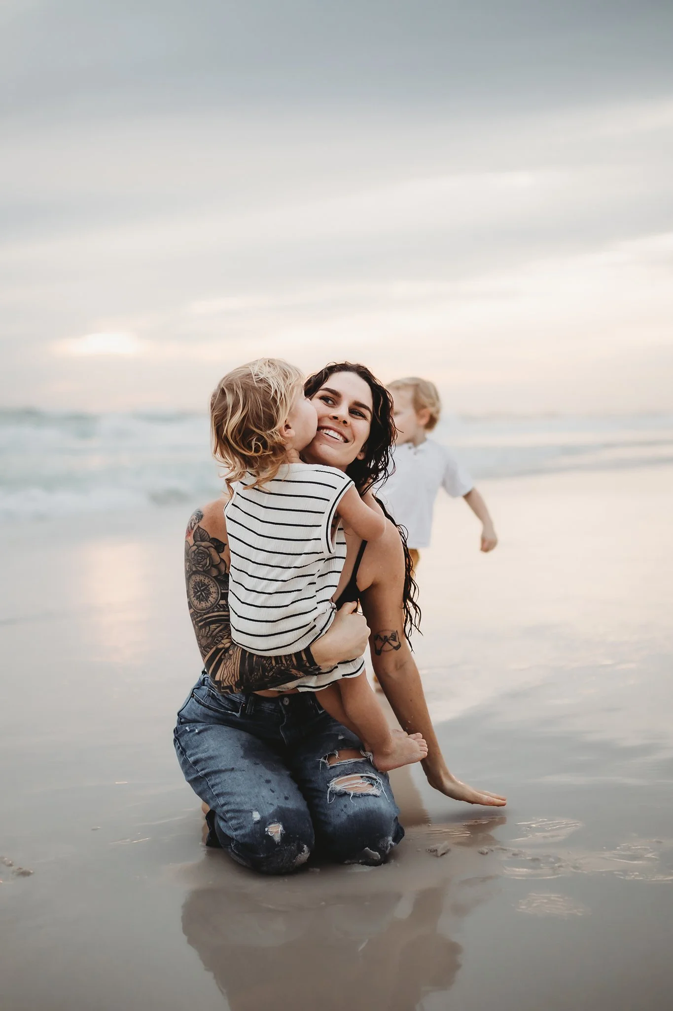 A mother holds her toddler son as they sit in the sand on the shore of the beach in Destin, Florida. Taken by Destin Photographer June Sunrise Photography.