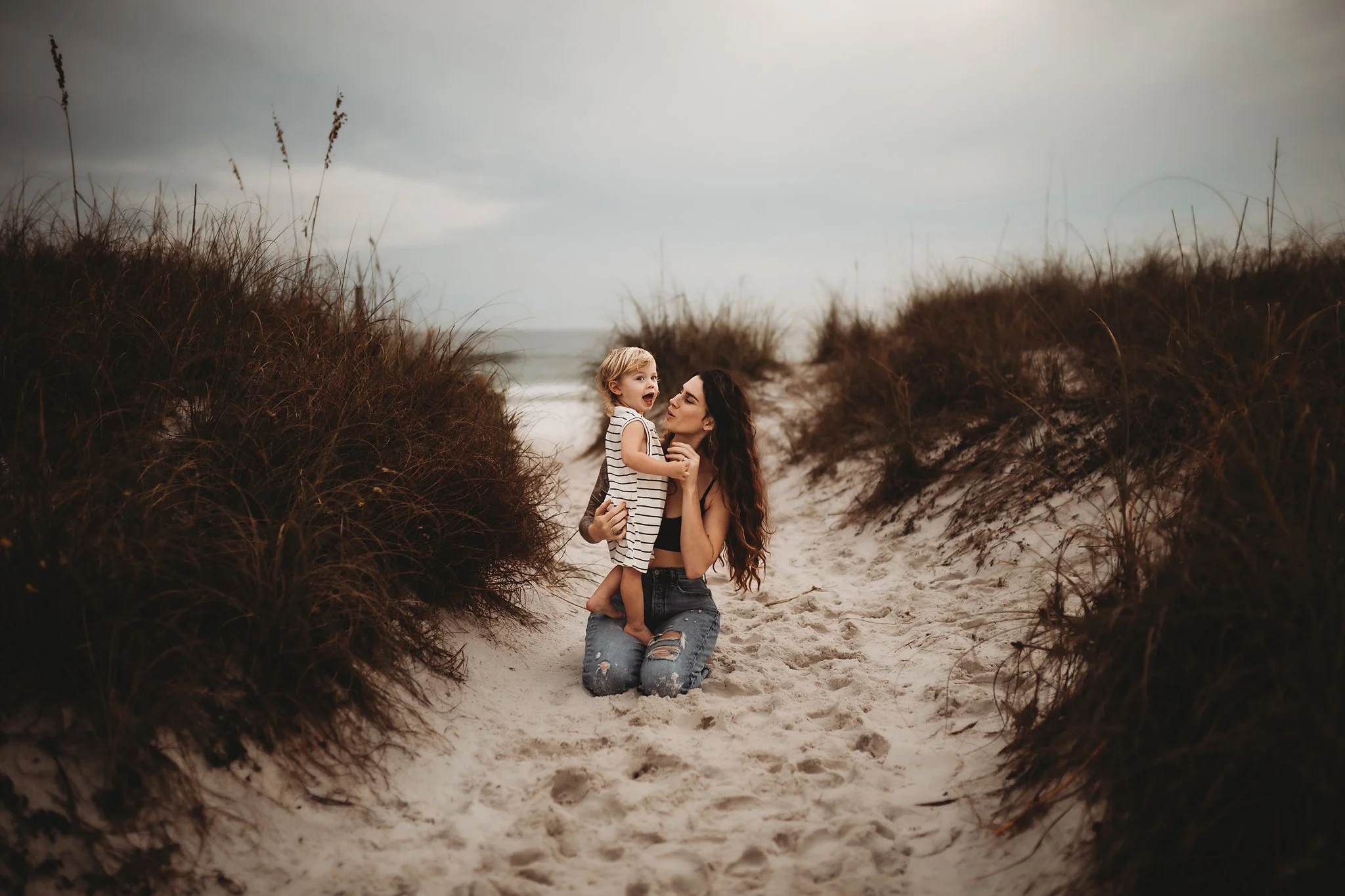 A mom holds her toddler son in between the dunes on the beach in Destin, Florida. Taken by Destin Photographer June Sunrise Photography.