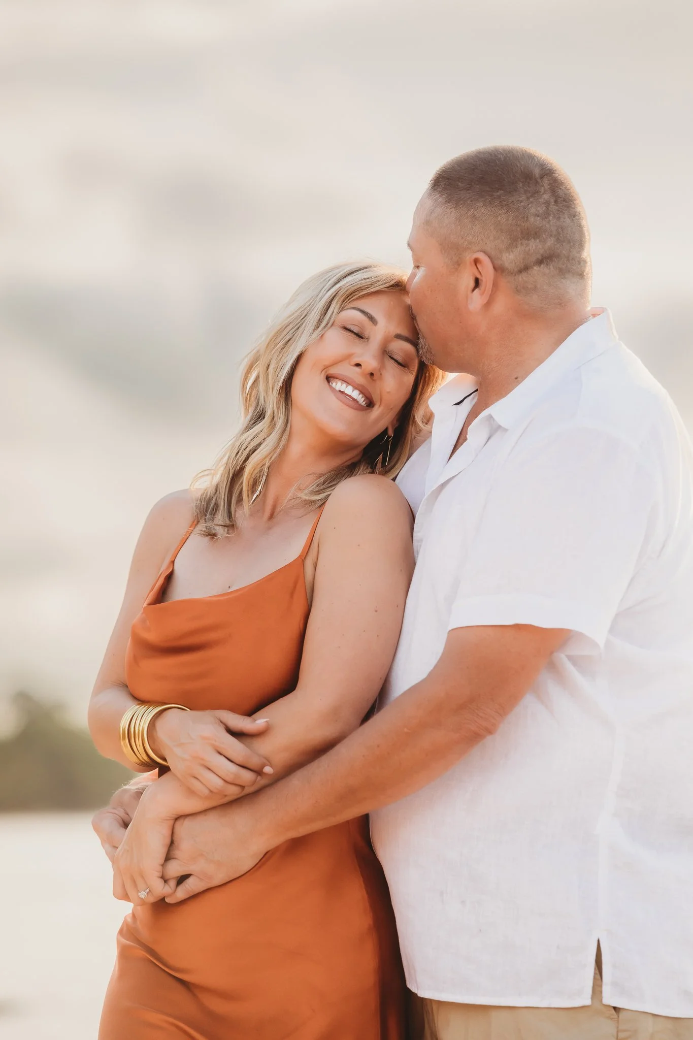 A couple snuggles as the man kisses the woman on the forehead in Destin, Florida. Taken by Destin Photographer June Sunrise Photography.