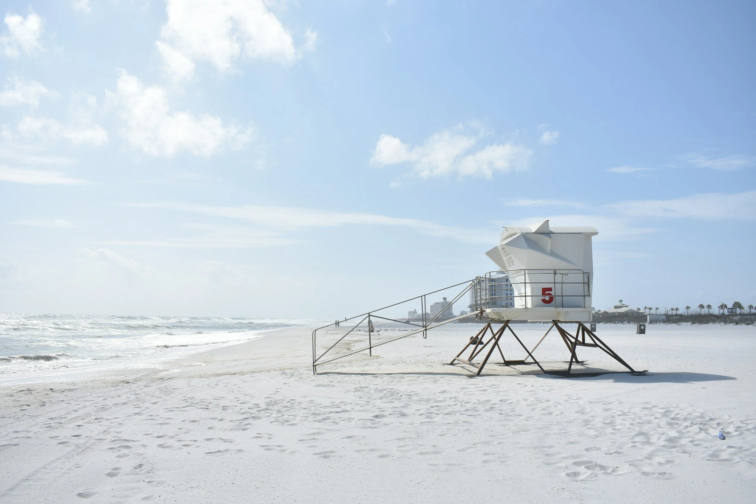 Empty lifeguard tower on a white sandy beach with the ocean waves and blue sky in the background.