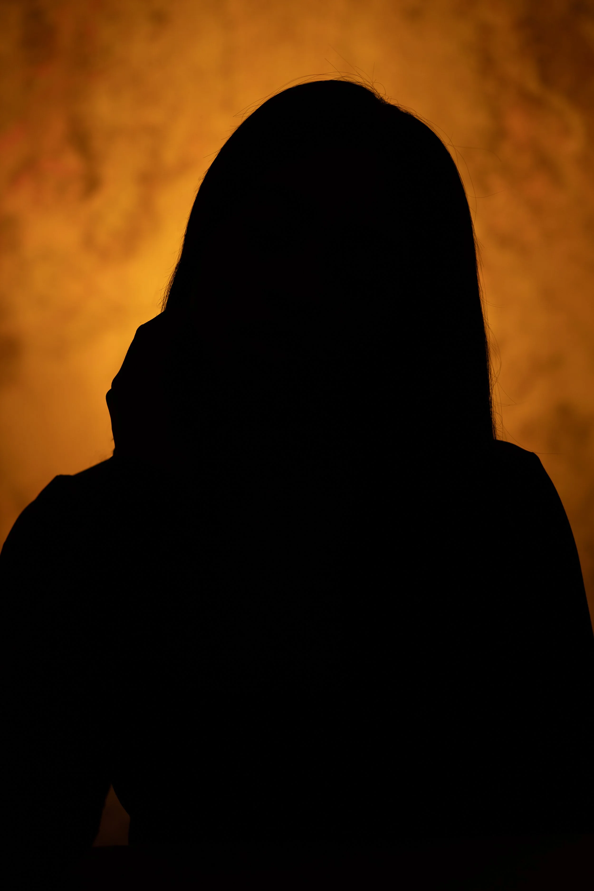 Silhouette of a person with long hair against a warm, textured orange background.
