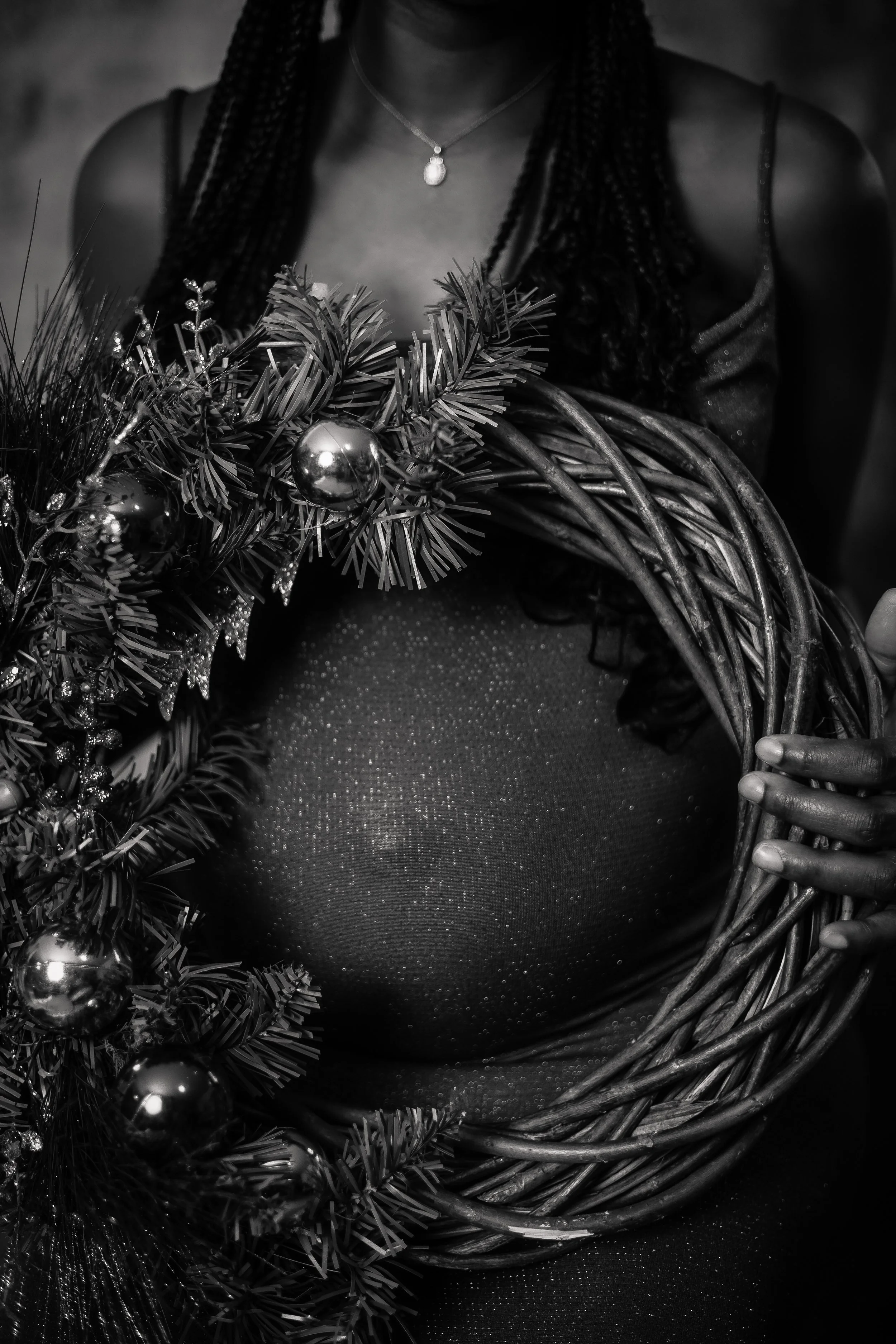 A woman holding a decorated Christmas wreath, dressed in a sparkly dress, with only her torso and necklace visible.