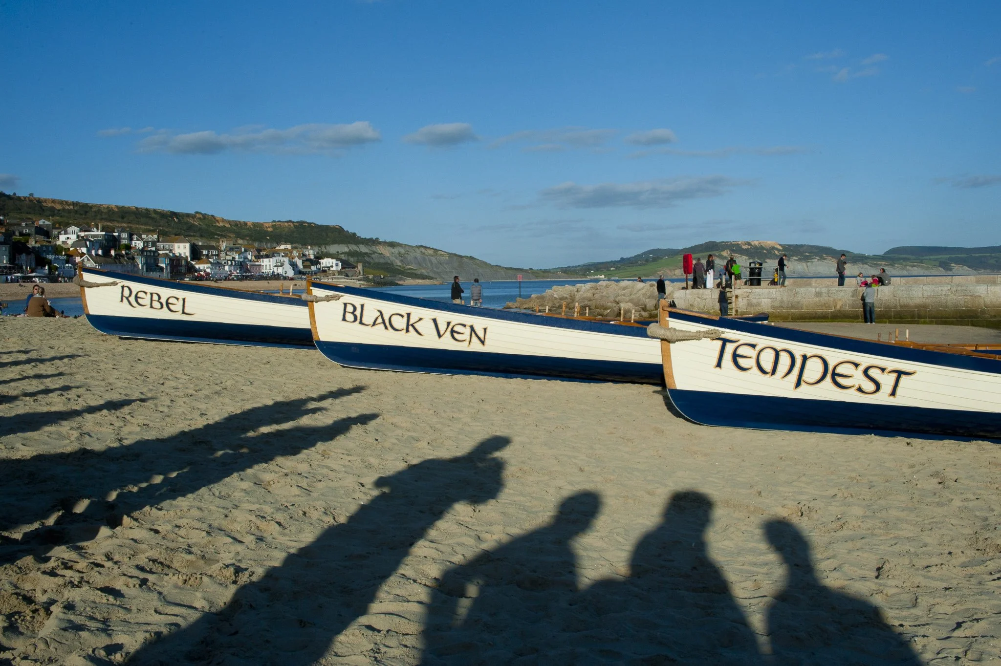 Three wooden gig boat resting on sunny sandy beach in Lyme Regis in Dorset