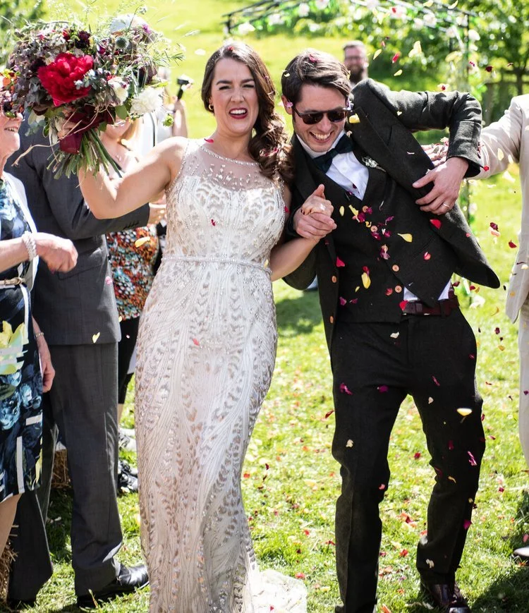 Bride with bouquet and Groom with sunglasses on walking down aisle of people throwing petals over them shot by Nick Matthews Photography who is an Affordable Wedding Photographer