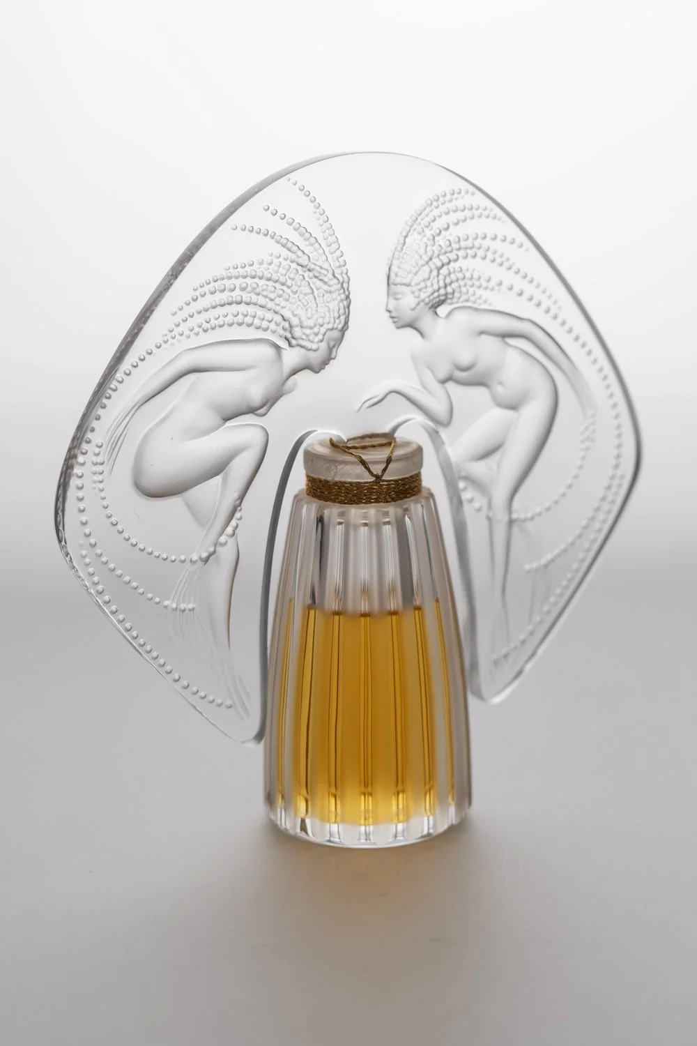 Decorative glass perfume bottle with two etched female figures and a small bottle of amber liquid in the center.