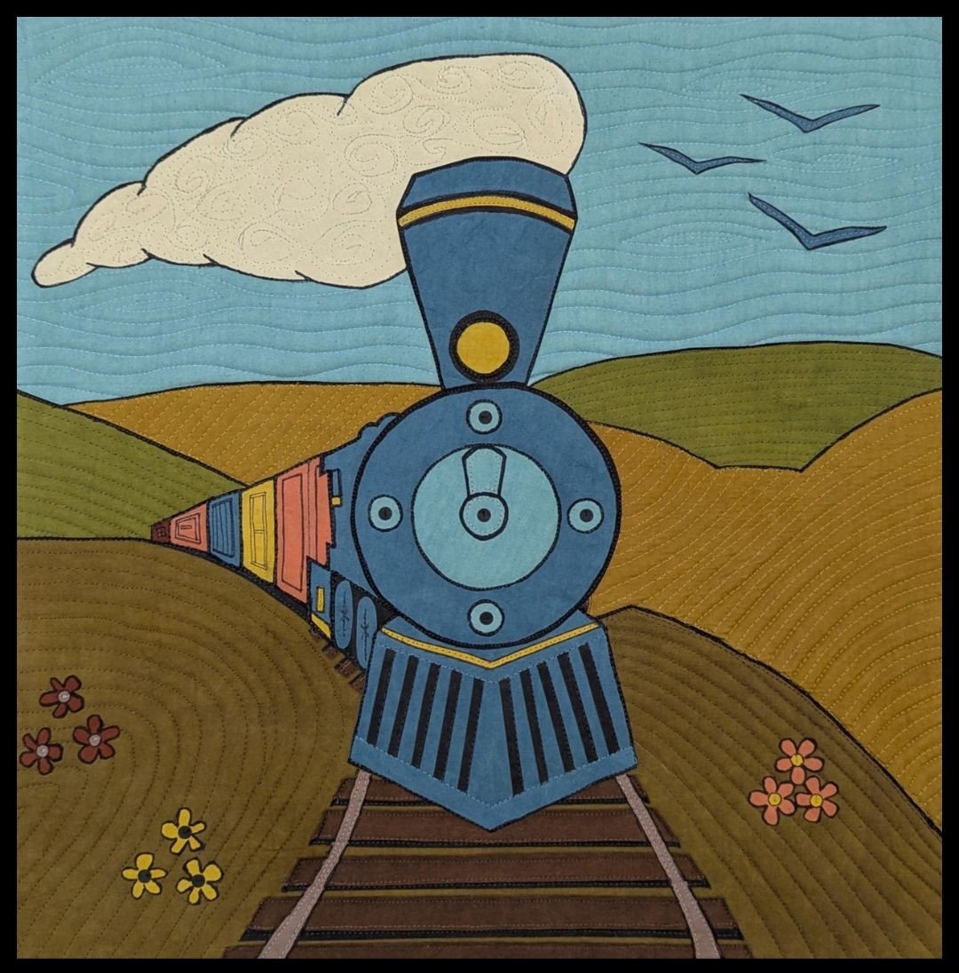 Colorful quilted fabric depicting a blue steam locomotive train on tracks, with rolling hills, a blue sky, clouds, flying birds, and flowers.