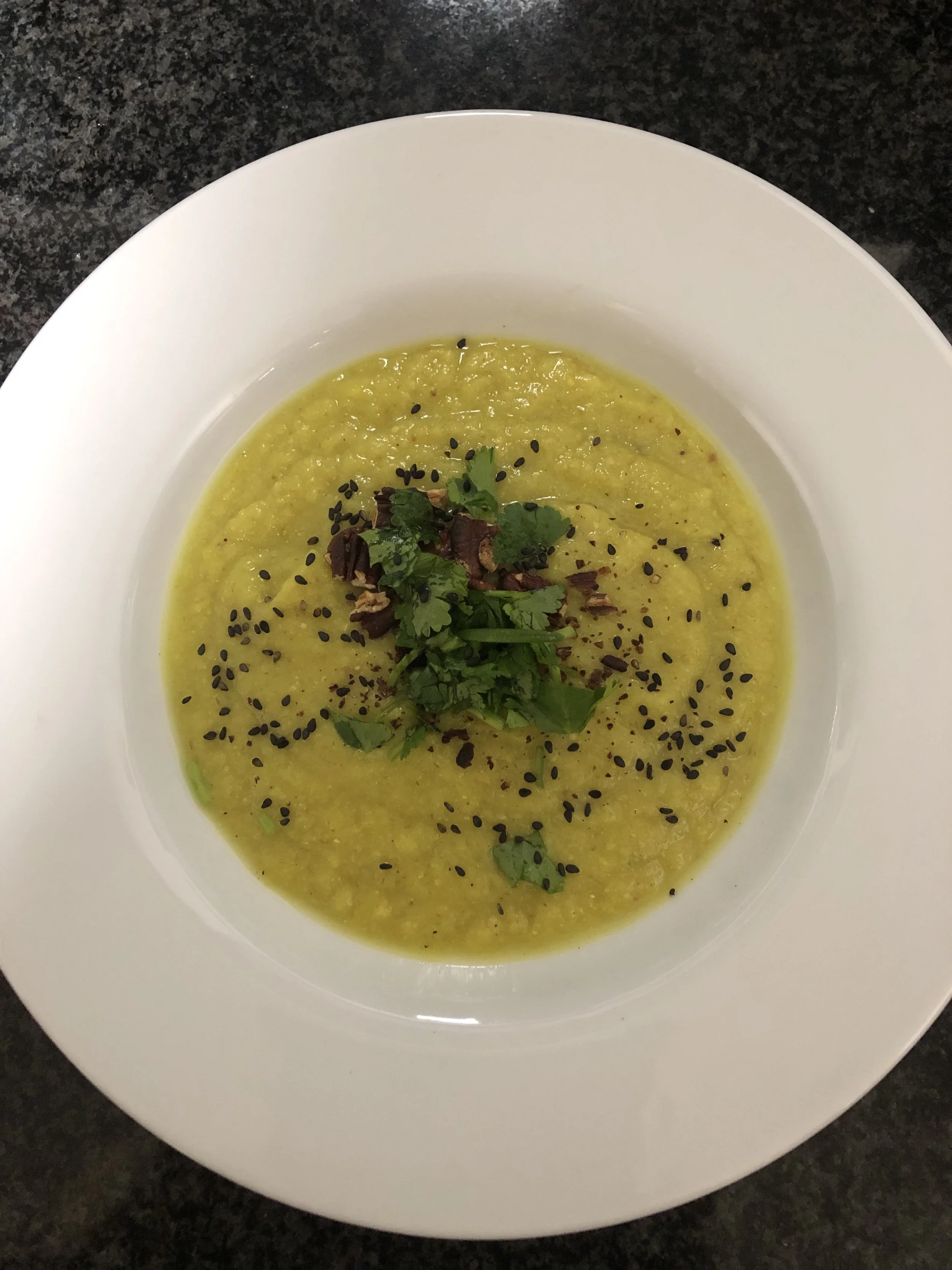 Grüne Linsensuppe in einer weißen Schale, garniert mit schwarzen Sesamsamen, frischen Kräutern und gerösteten Zwiebelstücken.