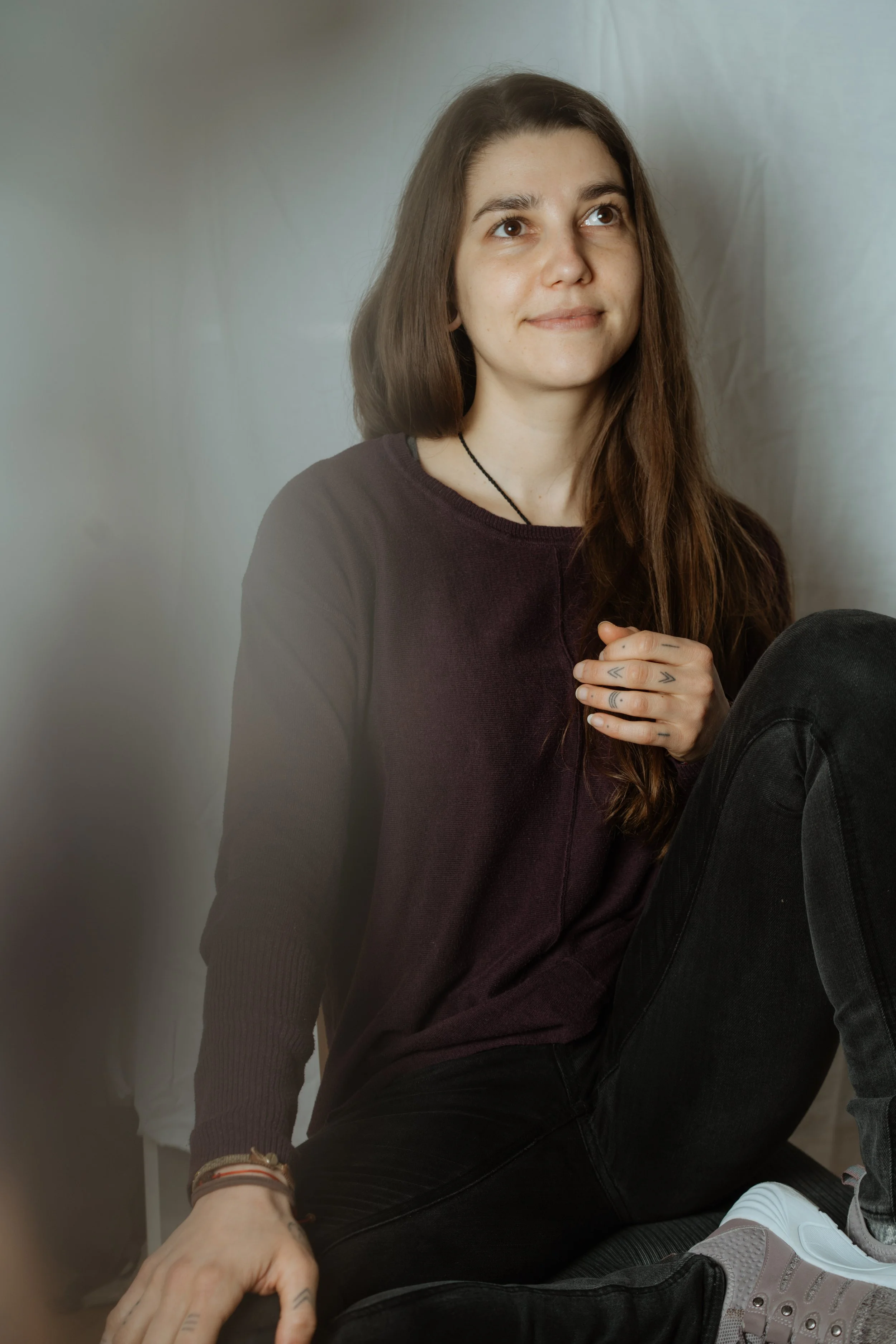 Eine junge Frau mit dunklen Haaren sitzt lächelnd im Schneidersitz.