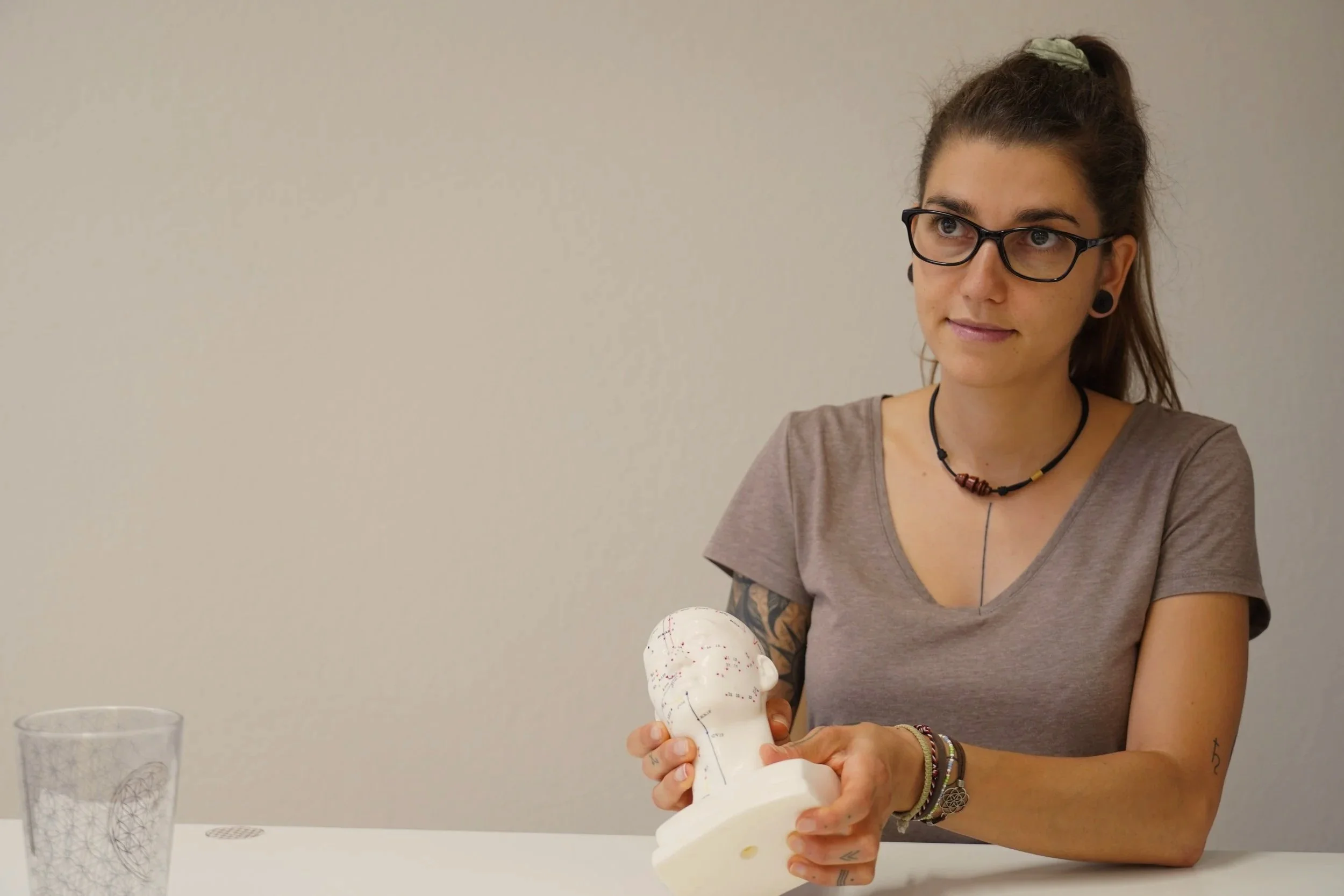 Eine junge Frau mit braunem Haar und Brille, die an einem Modell eine naturheilkundliche Methode demonstriert.