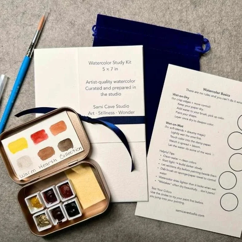 Watercolor study kit with a palette of paints, two sheets with instructions, a brush, and a blue carrying case on a gray surface.