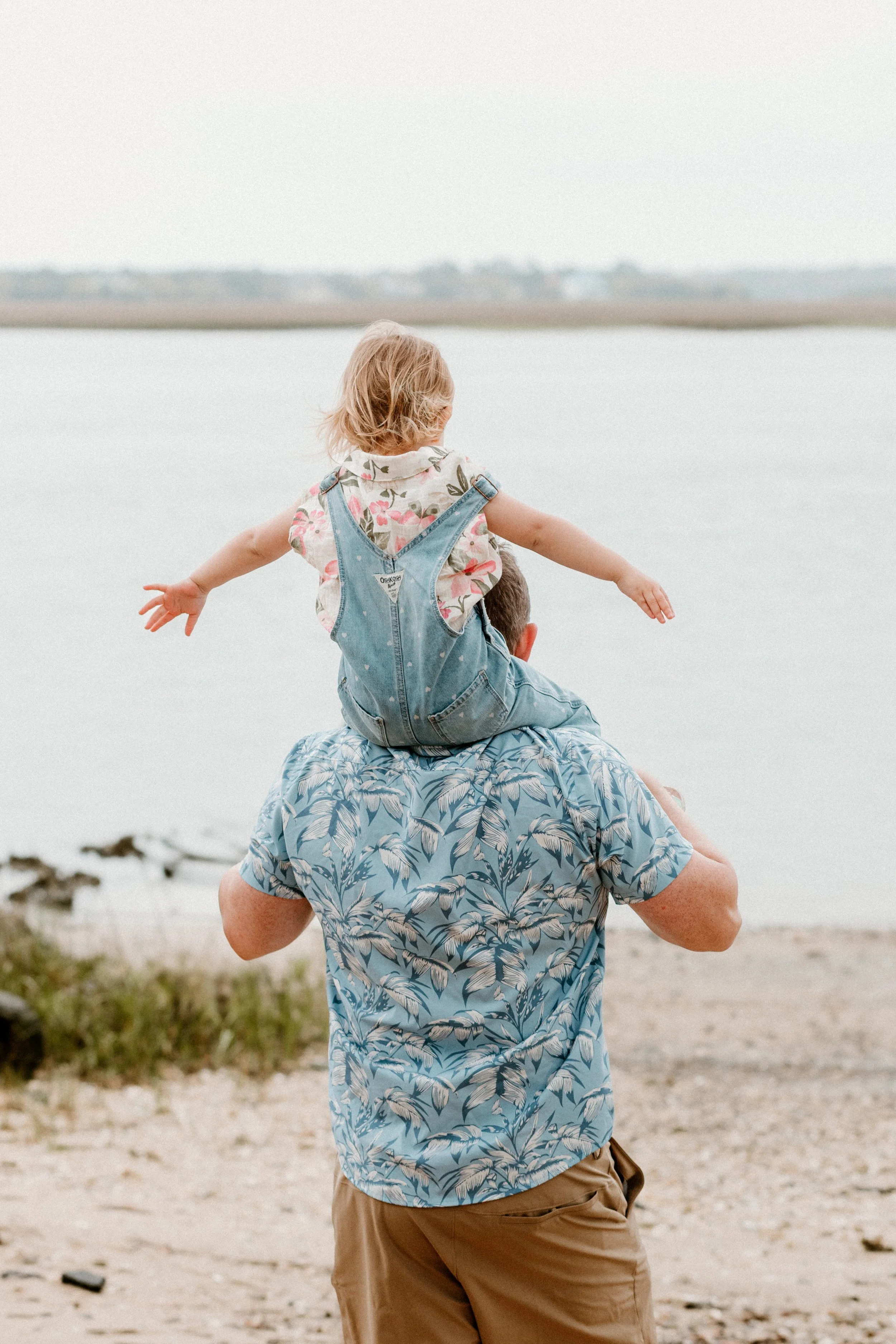 Father carrying young child on shoulders during relaxed family portrait session outdoors
