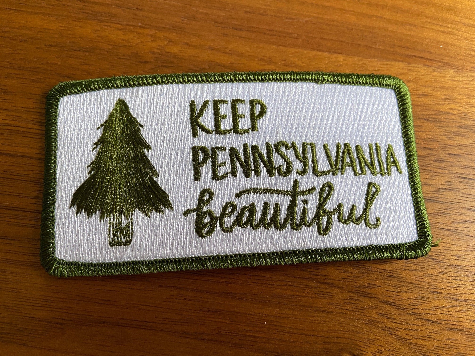 Stitched patch with White background with a hand drawn tree and Keep Pennsylvania Beautiful text in green thread.