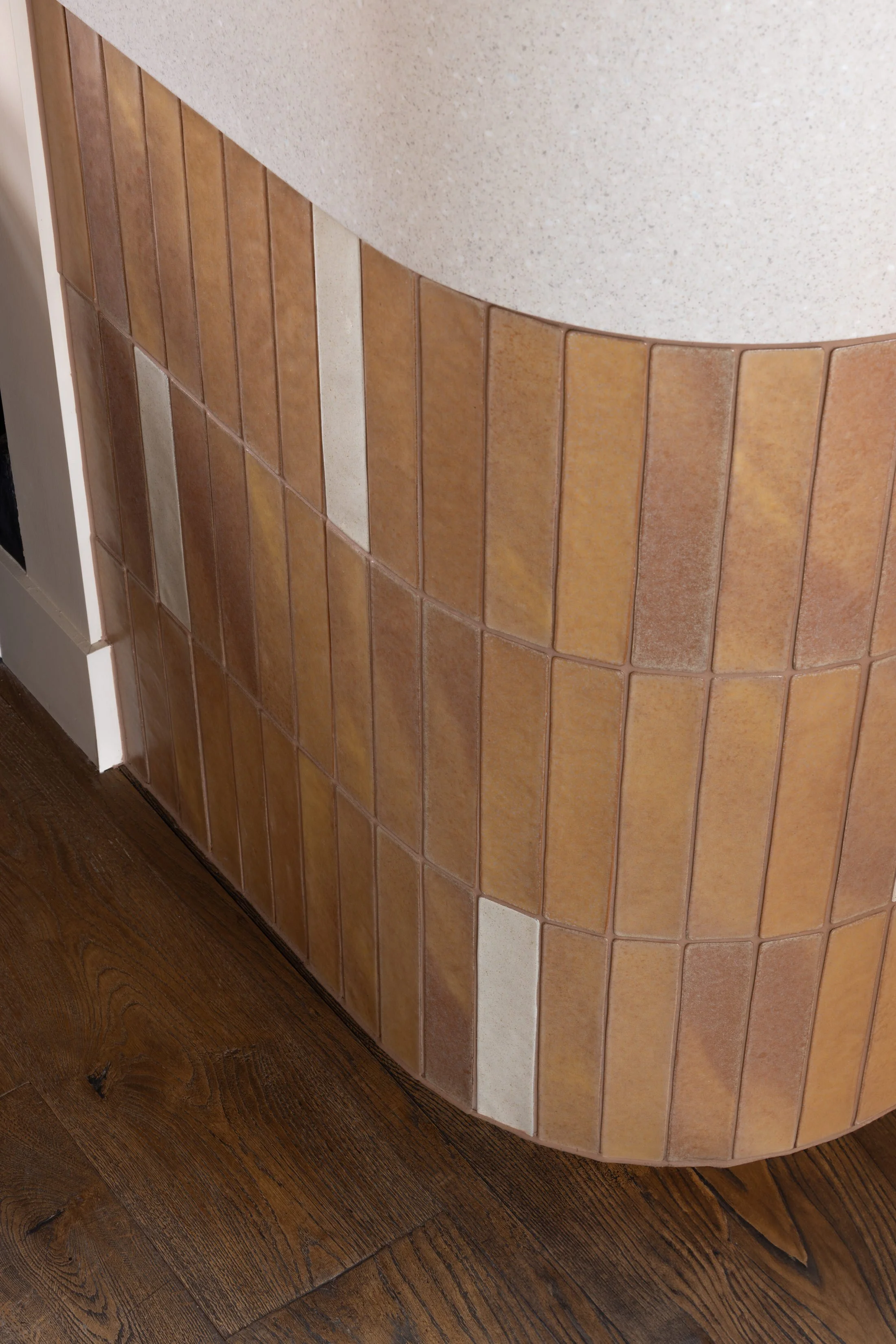 Close-up of a tiled countertop with brown and beige tiles, curved edge, and wooden flooring below.