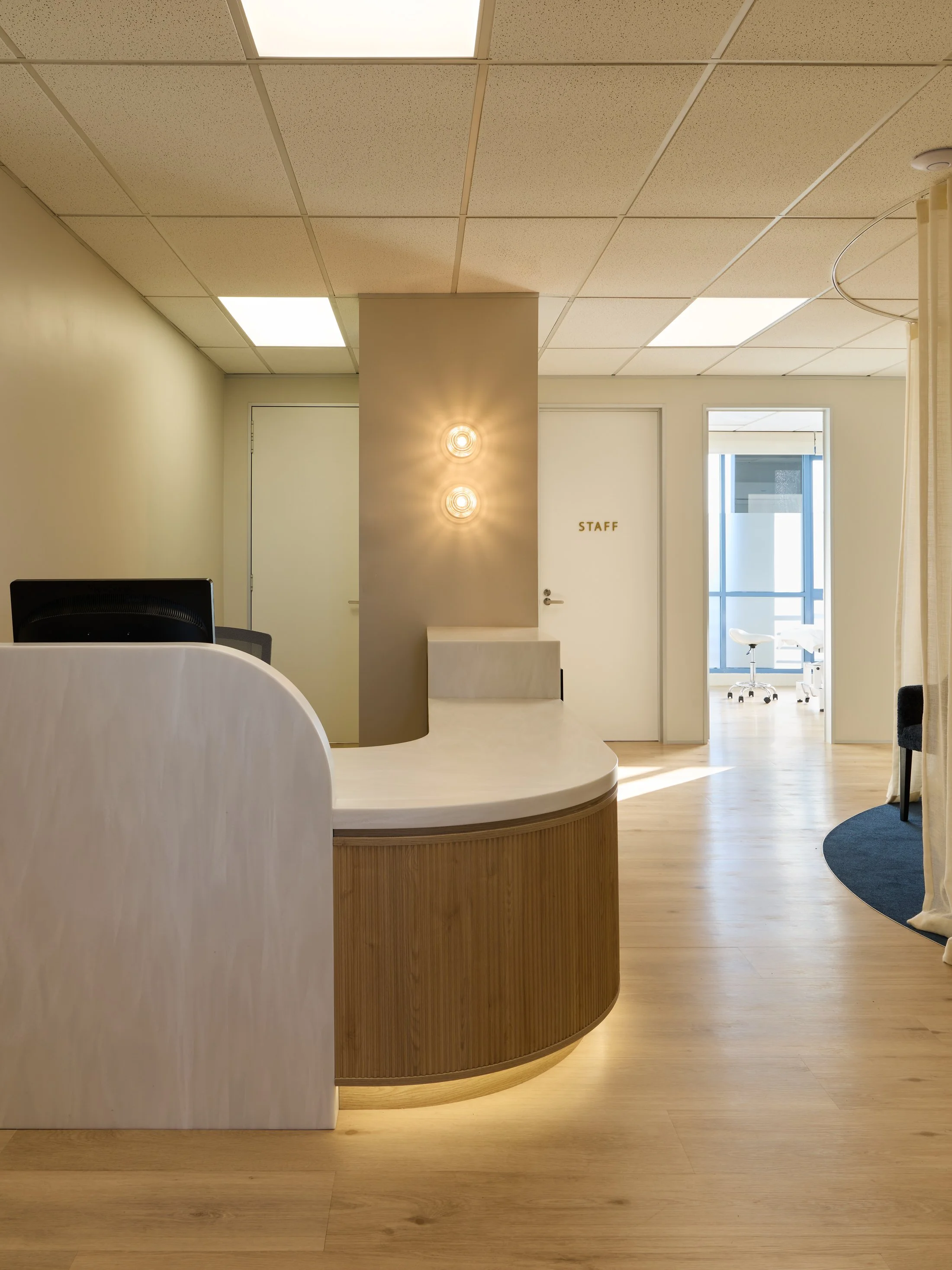 Indoor space with a reception desk, a wall with three lights, a door with a "STAFF" sign, and a small area with a stool near a window.