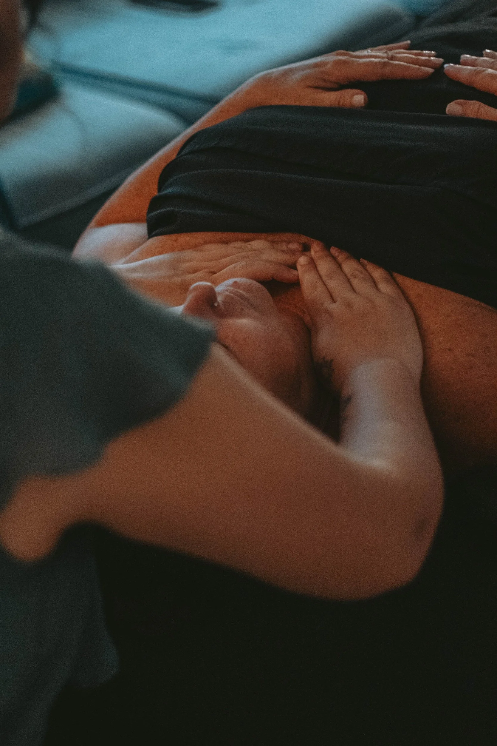 Close-up of a person's hand resting on their stomach, with another hand gently touching the hand. The person is wearing a black shirt, and the background appears to be a blue fabric surface.