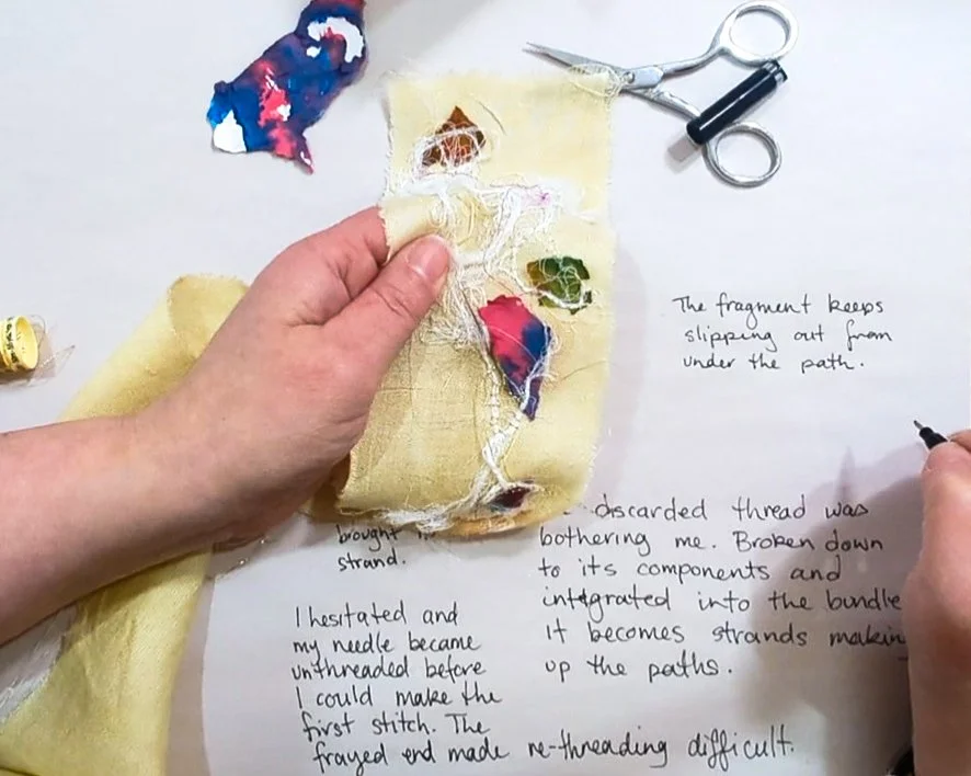 Hands holding a stitched fabric piece while writing notes on a large sheet of paper.