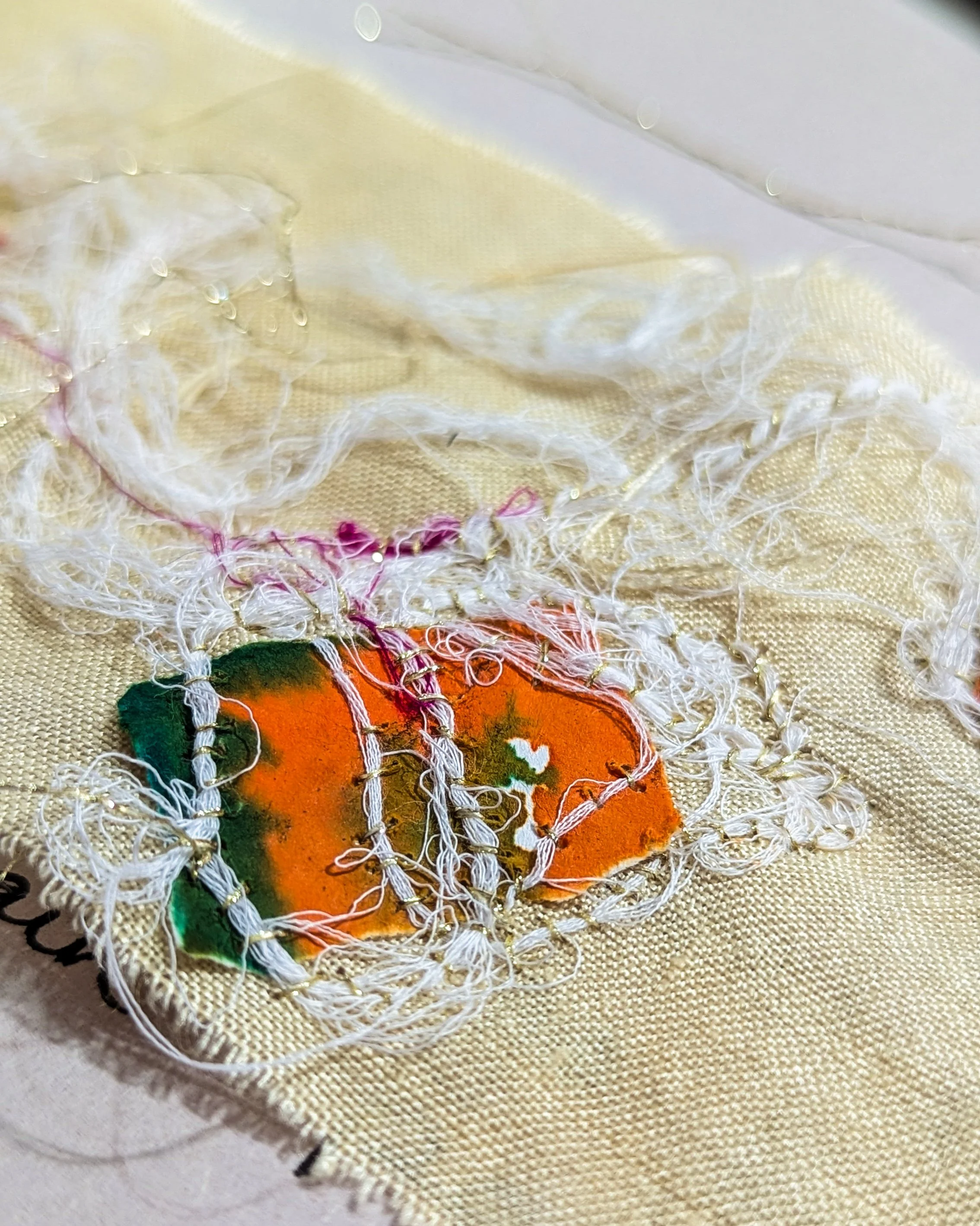 Close-up of layered fabric fragments stitched with white and gold threads.