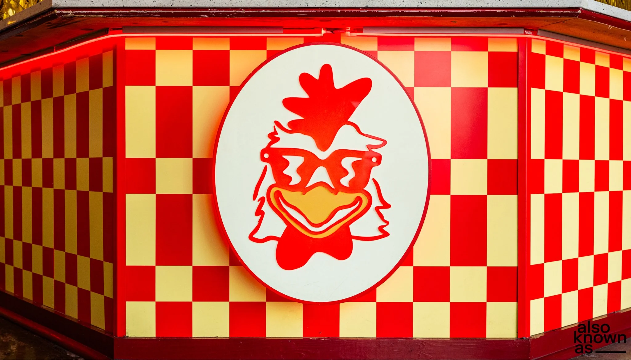 A bright red and yellow checkered wall with a large circular sign featuring a stylized cartoon chicken wearing sunglasses and a hat.