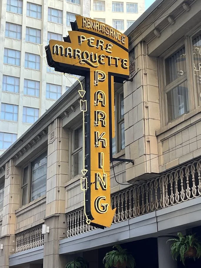 Vintage vertical neon sign attached to the side of a building in an urban area with other tall buildings visible in the background.
