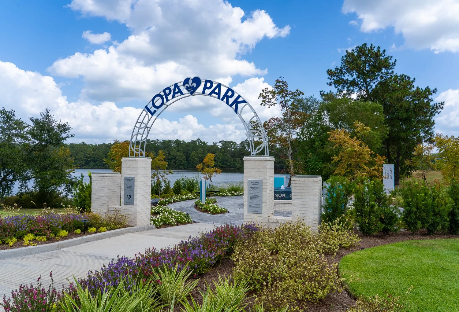 Entrance arch to Lopa Park with a large lake and trees in the background, surrounded by colorful flowers and shrubs.