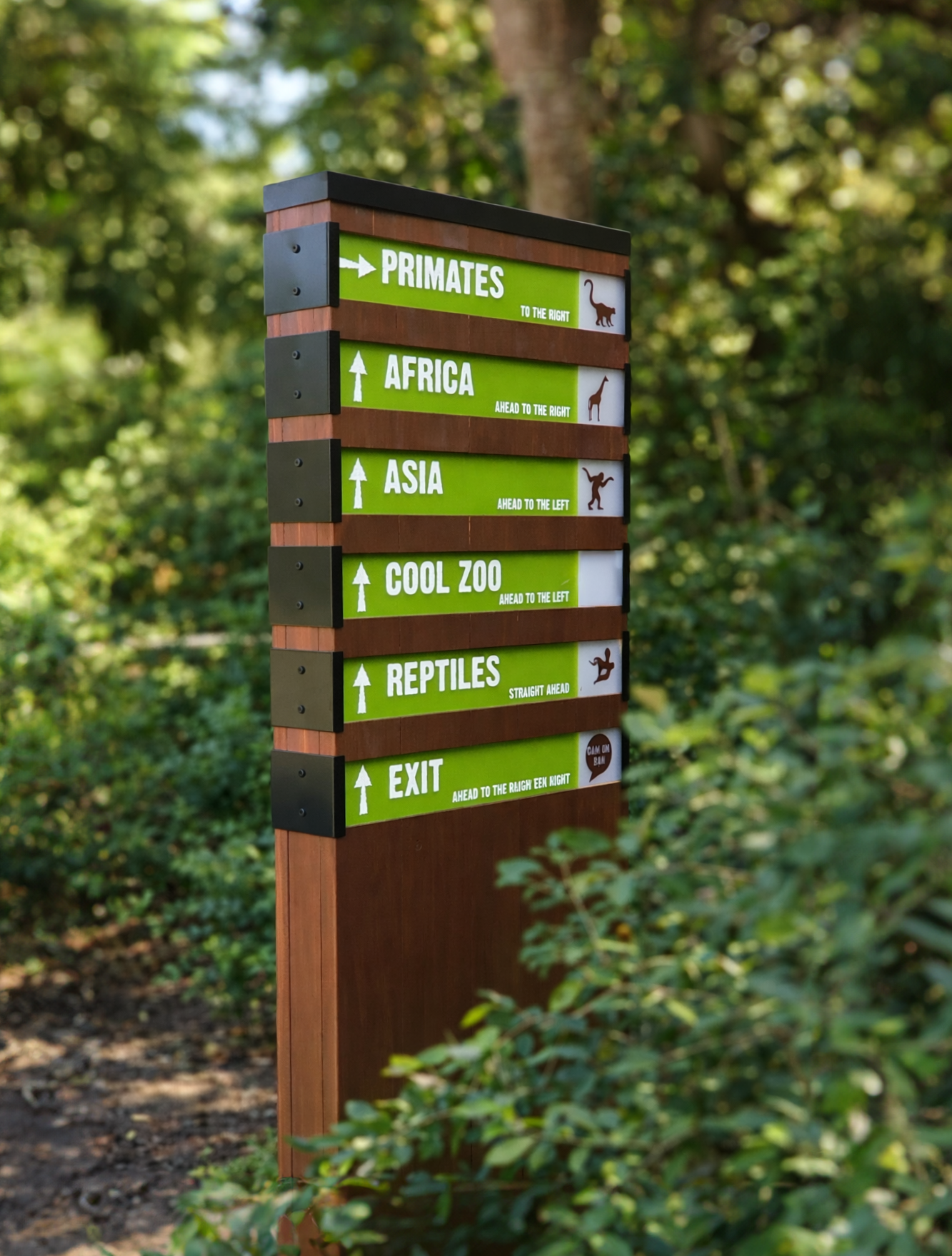 A wooden trail sign with green and white directional markers for a zoo, including primates, Africa, Asia, reptiles, and an exit, each with directional arrows and labels, situated in a forest environment.