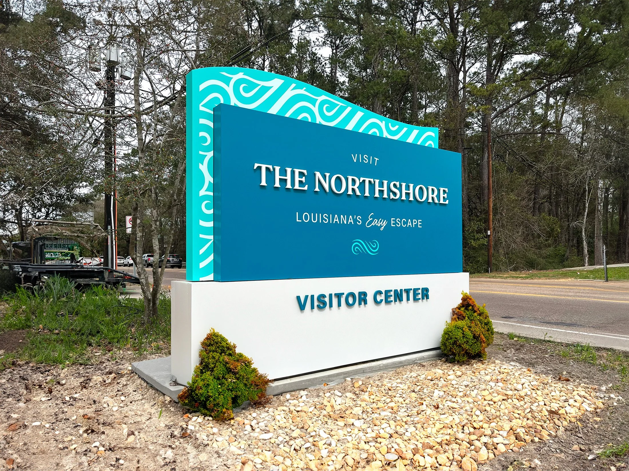 Sign for The Northshore Visitor Center in Louisiana, with trees and road in the background.