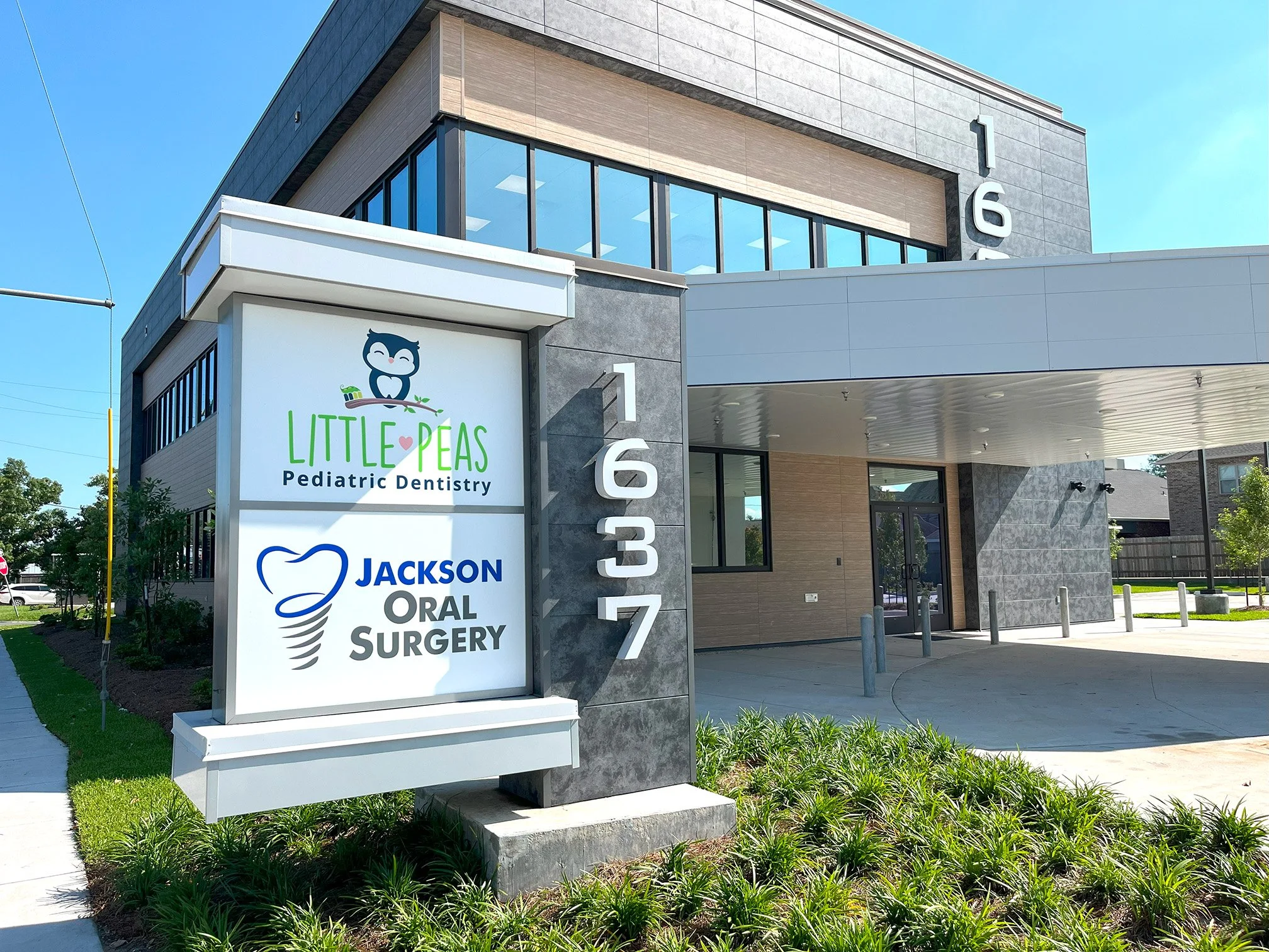 Modern building with signs for Little Peas Pediatric Dentistry and Jackson Oral Surgery at 1637, with a sidewalk and landscaped greenery outside.